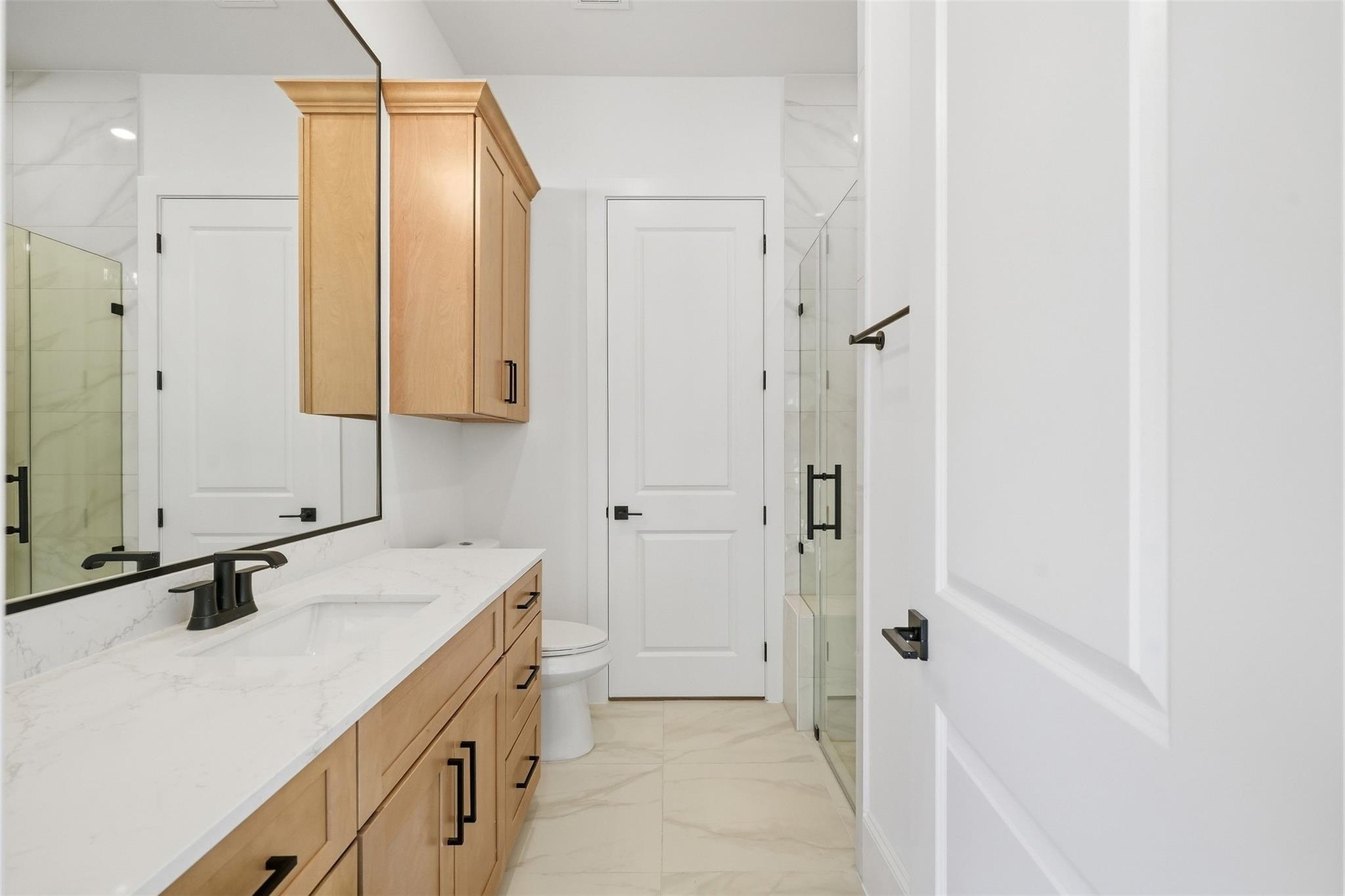 Bathroom with a light wood vanity, marble-look counter, black fixtures, and glass shower.