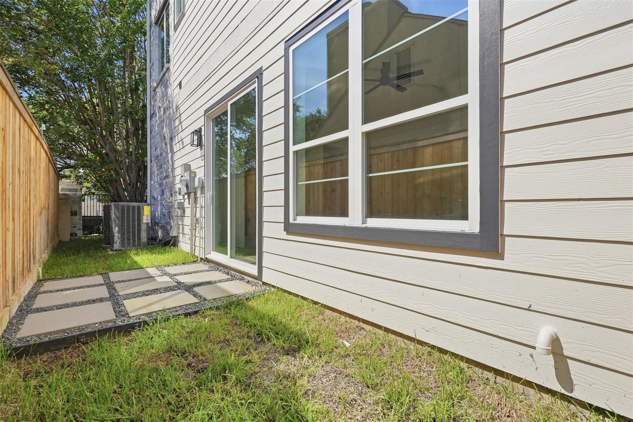Side yard with a stepping-stone patio beside the house’s large windows and sliding glass door.