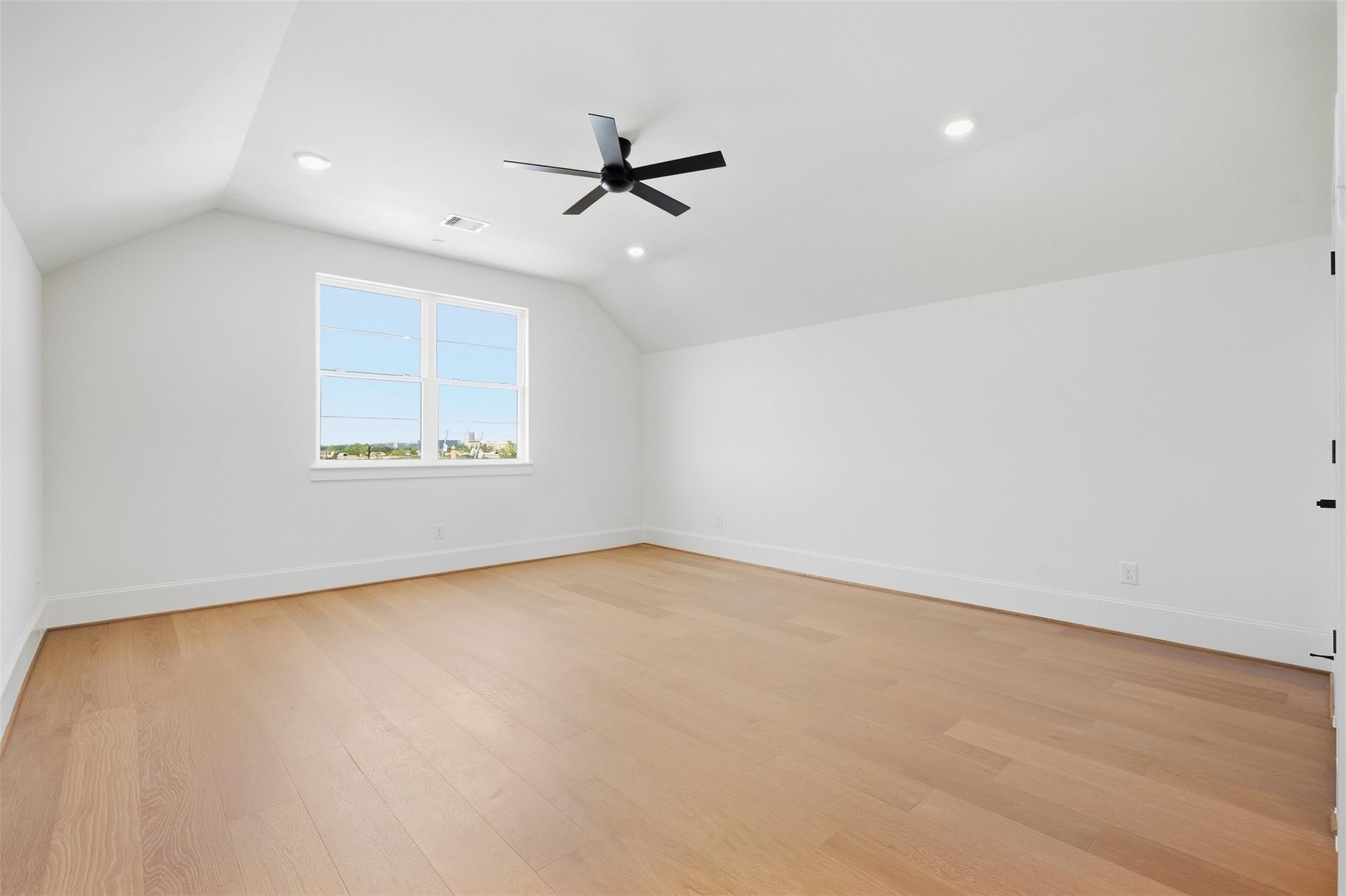 Empty room with light wood flooring, a sloped ceiling, and a double window.