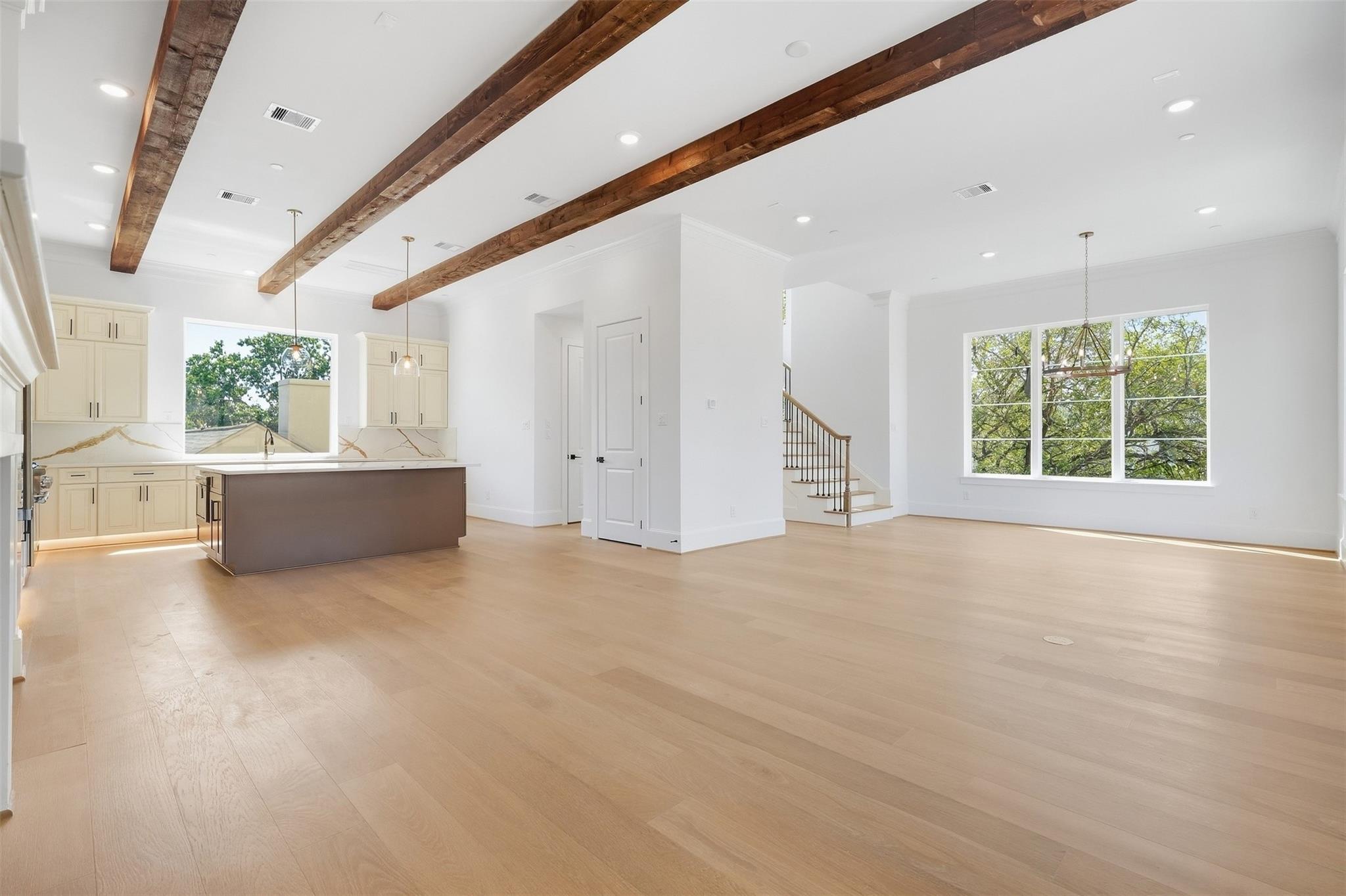 Open-plan kitchen and living area with exposed wood beams, a large island, and wide windows.