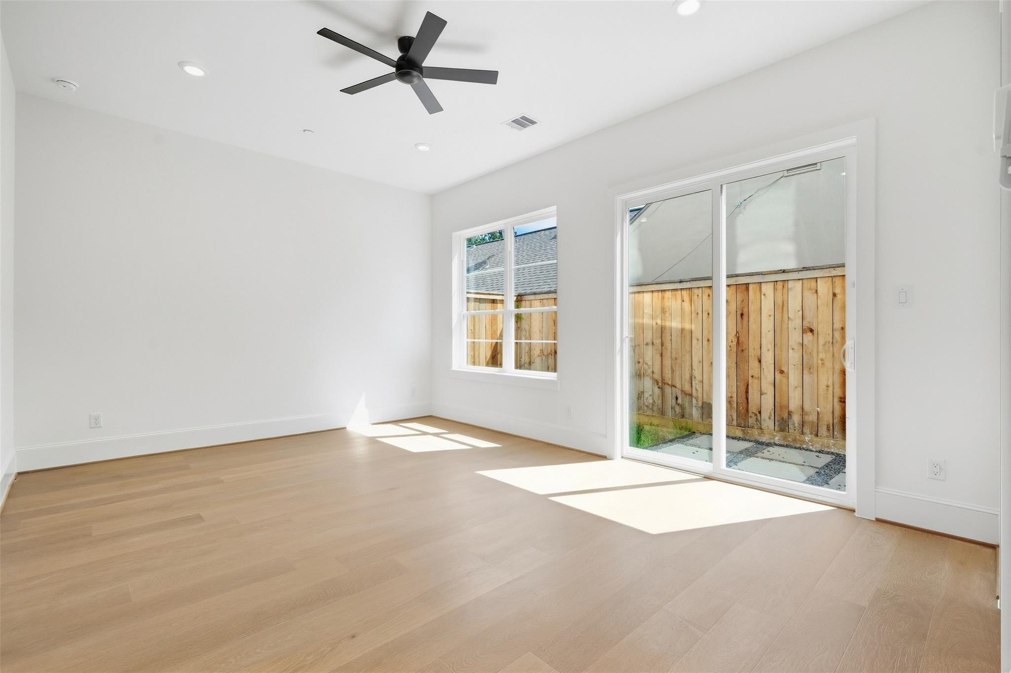 Vacant room with light wood floors, a black ceiling fan, and a sliding glass door to a fenced patio.