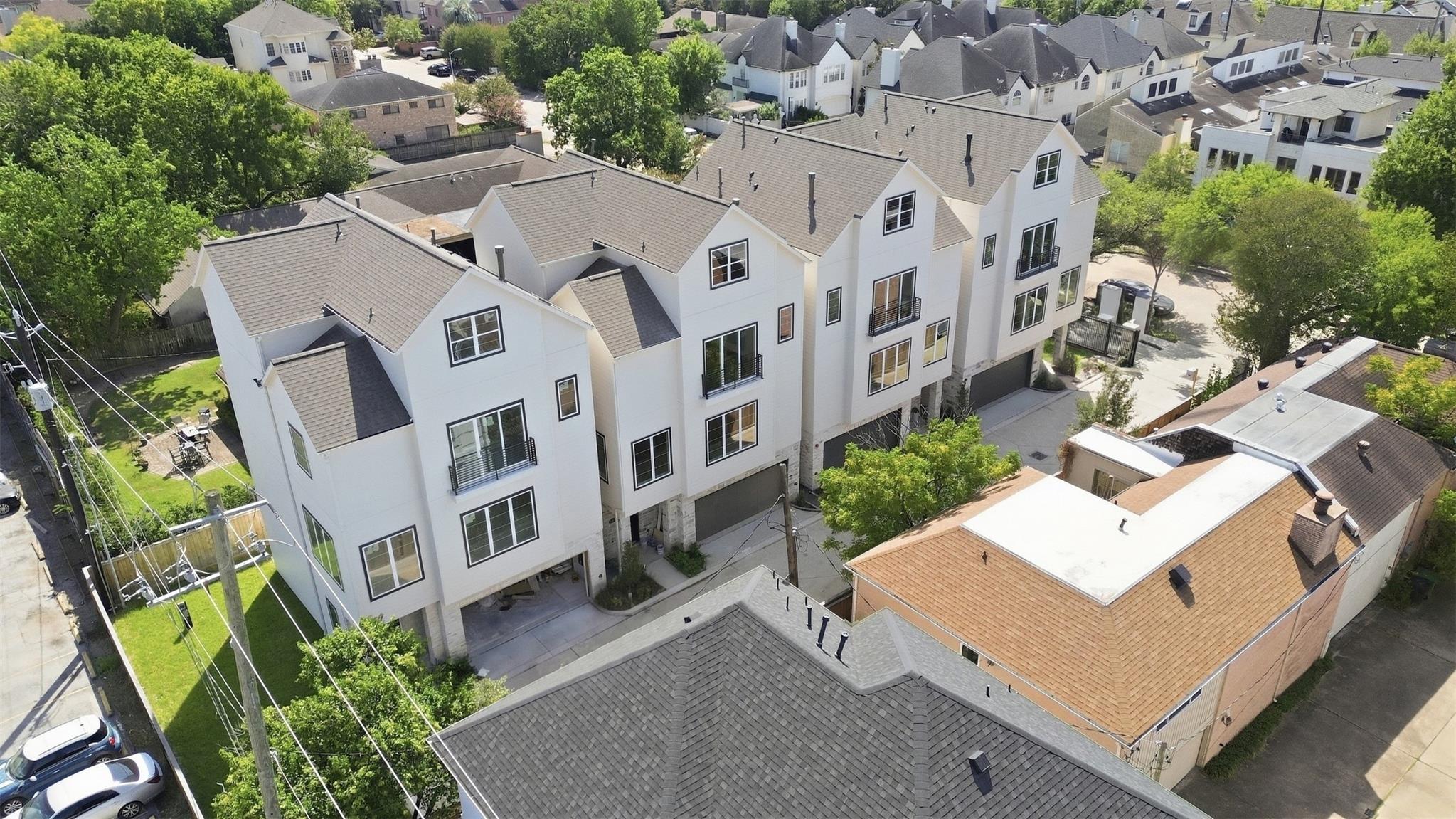 Aerial view of modern white townhomes with balconies and garages among leafy Houston homes.