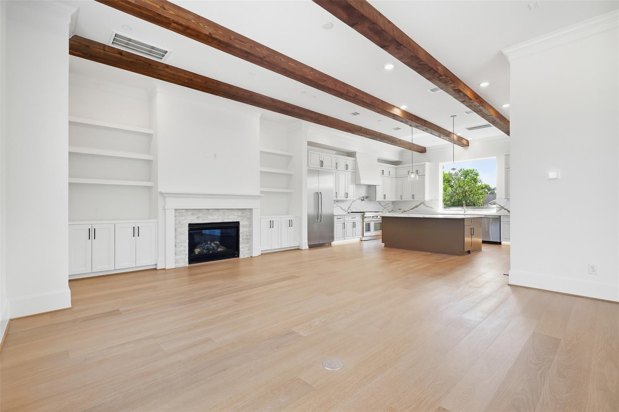 Open kitchen and living area with exposed wood beams, a stone fireplace, and a large island.