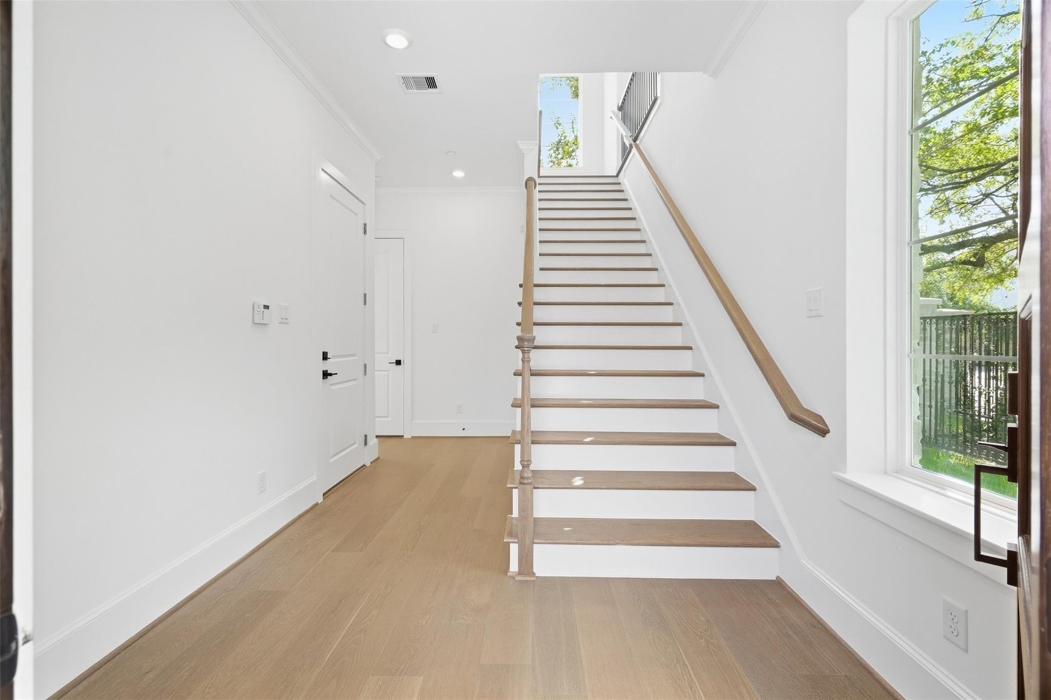 Entry hall with a wood-railed staircase, light wood floors, and a large window.