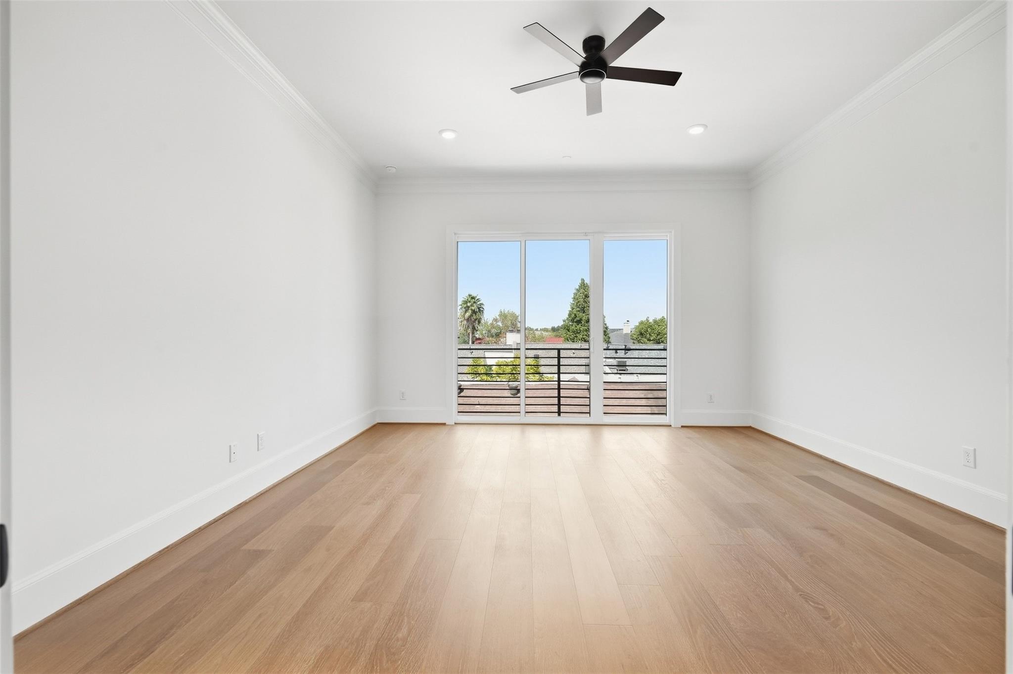 Vacant room with light wood floors, a ceiling fan, and sliding doors to a balcony.
