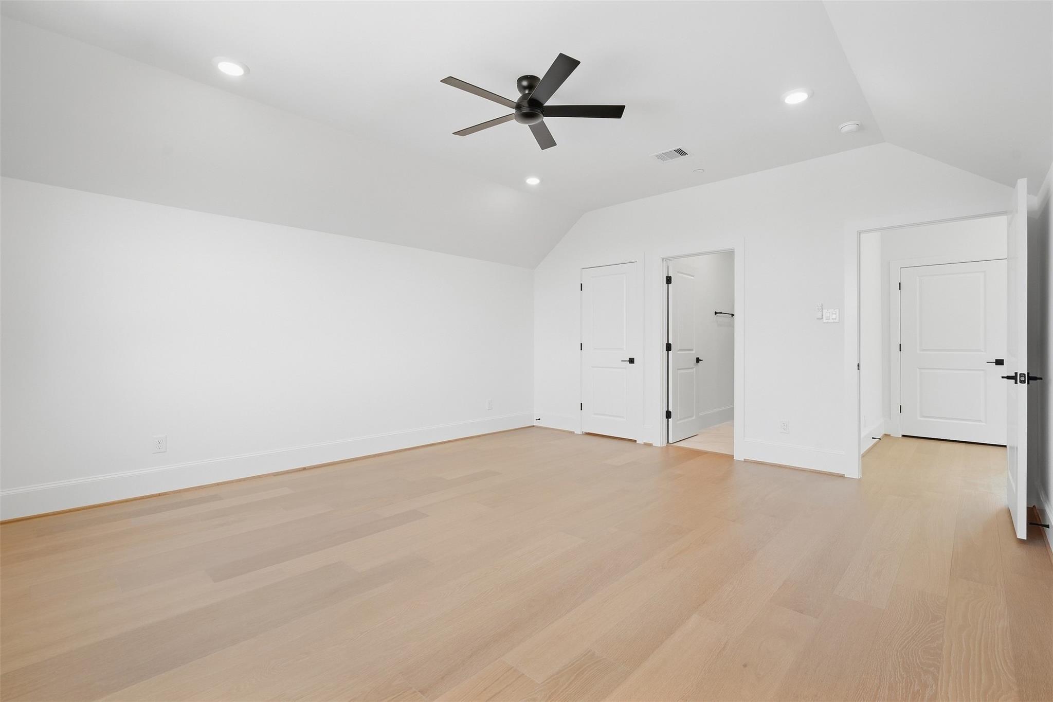 Vacant room with light wood floors, a vaulted ceiling, and a black ceiling fan.
