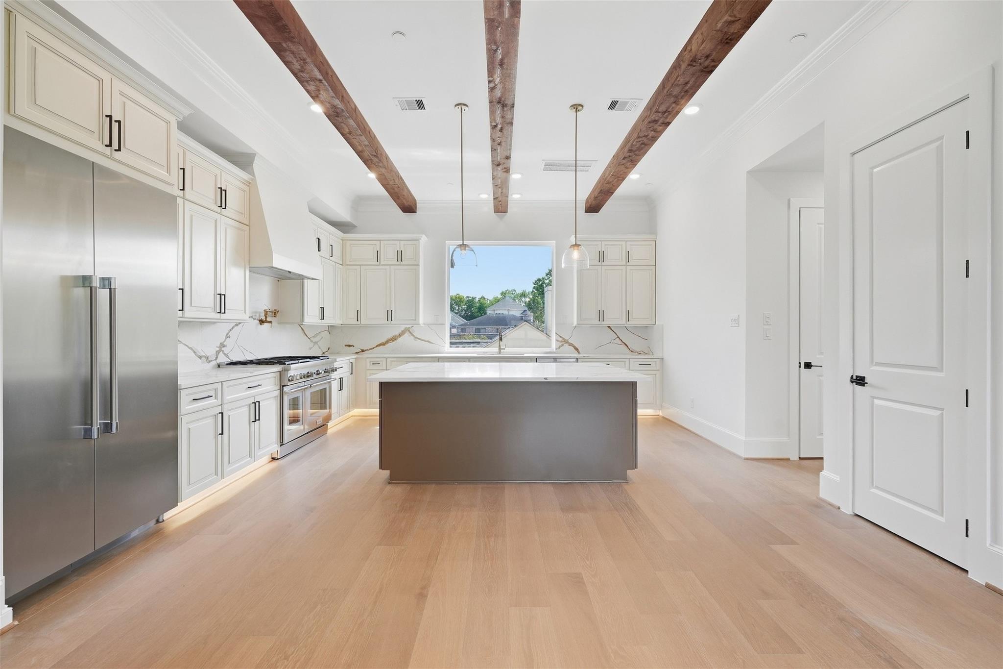 Kitchen with a large gray island, white cabinets, stainless appliances, and exposed wood ceiling beams.
