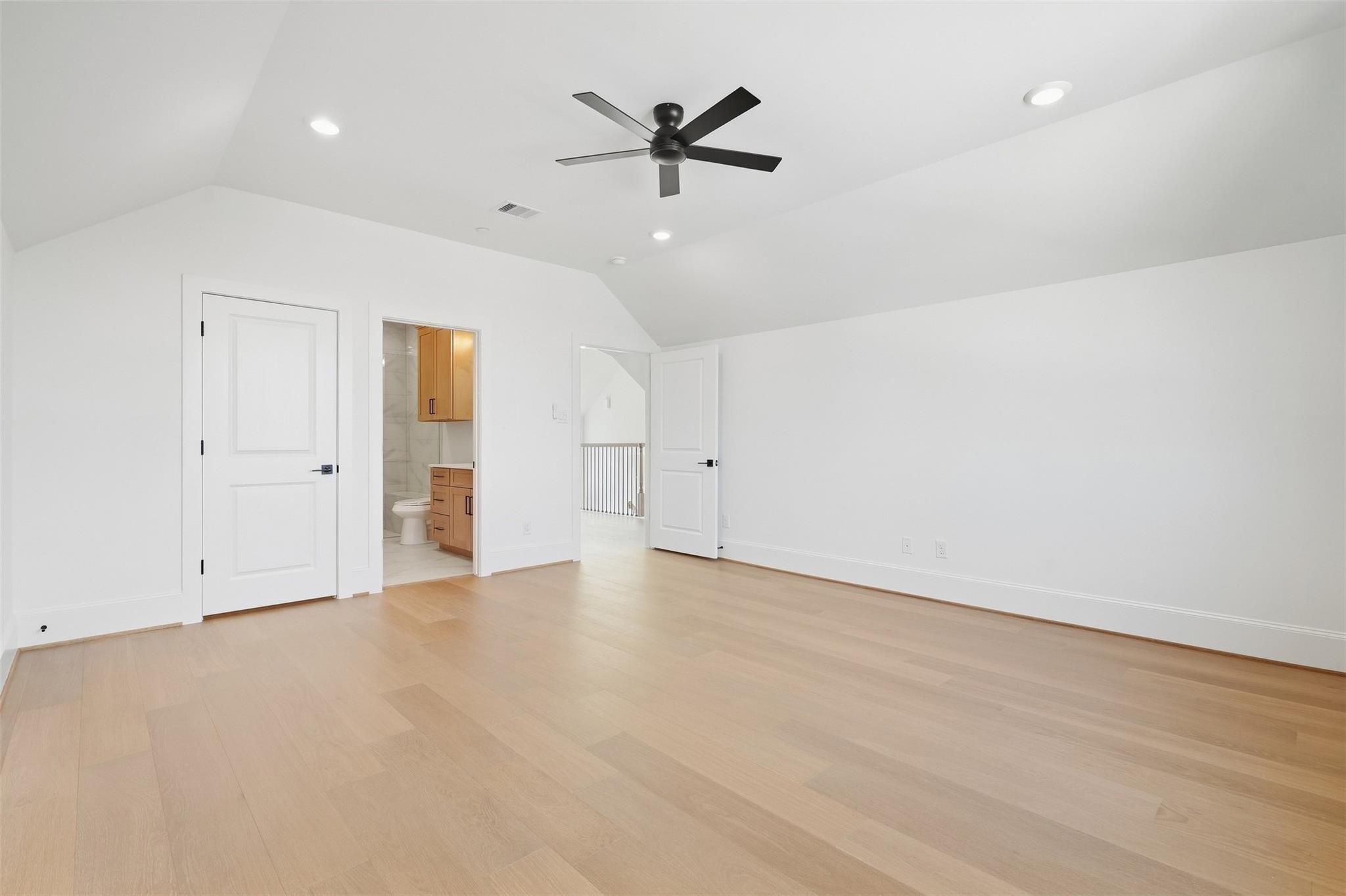 Empty bedroom with sloped ceiling, light wood floors, and a black ceiling fan.