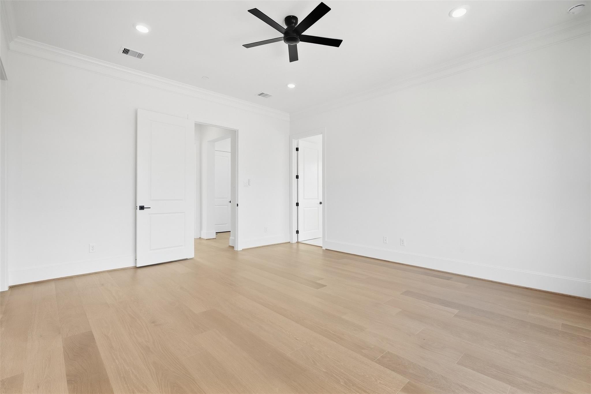 Empty room with light wood flooring, white walls, and a black ceiling fan.