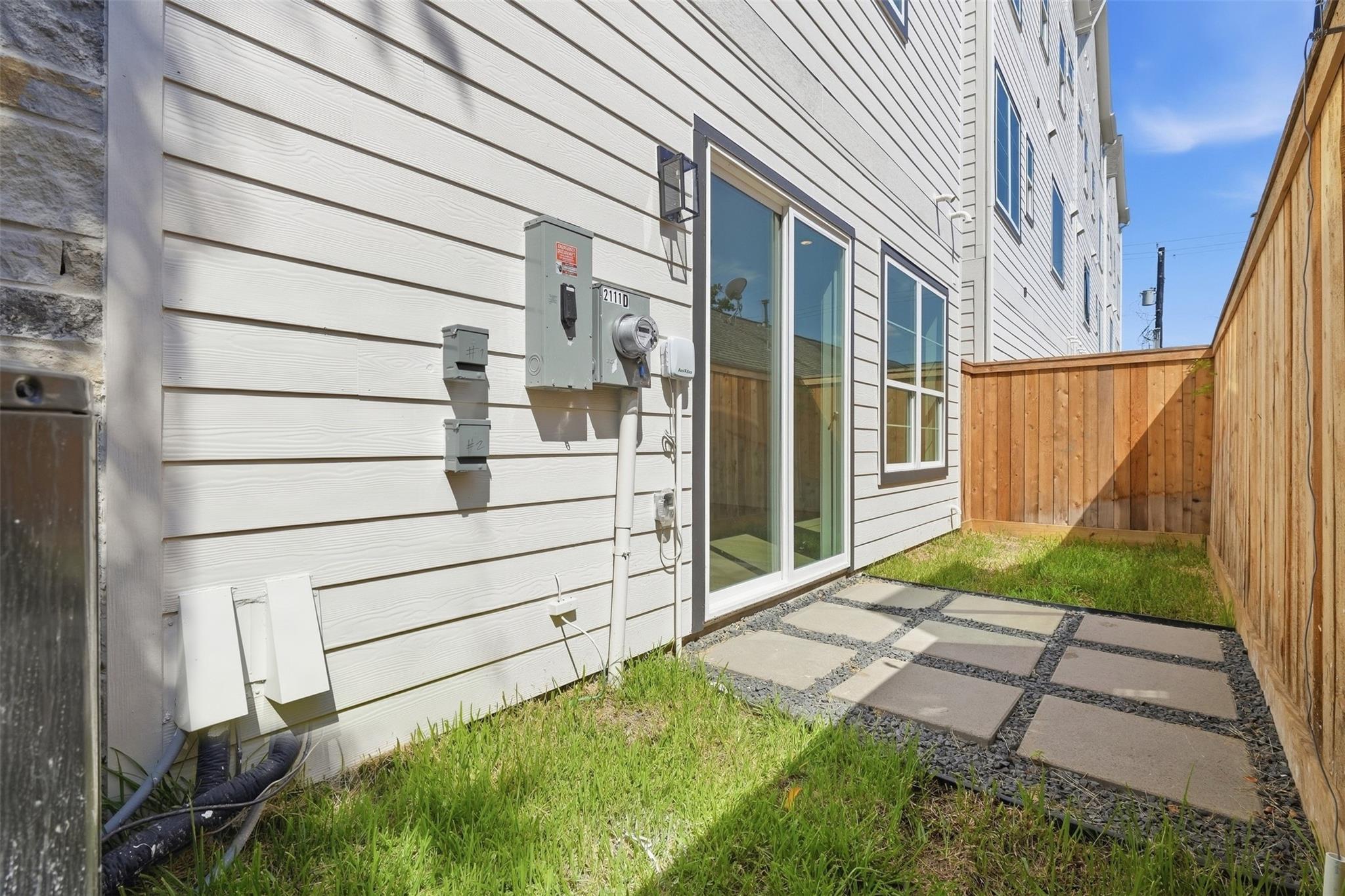 Fenced side yard with a stepping-stone path beside a white-sided home and sliding glass door.