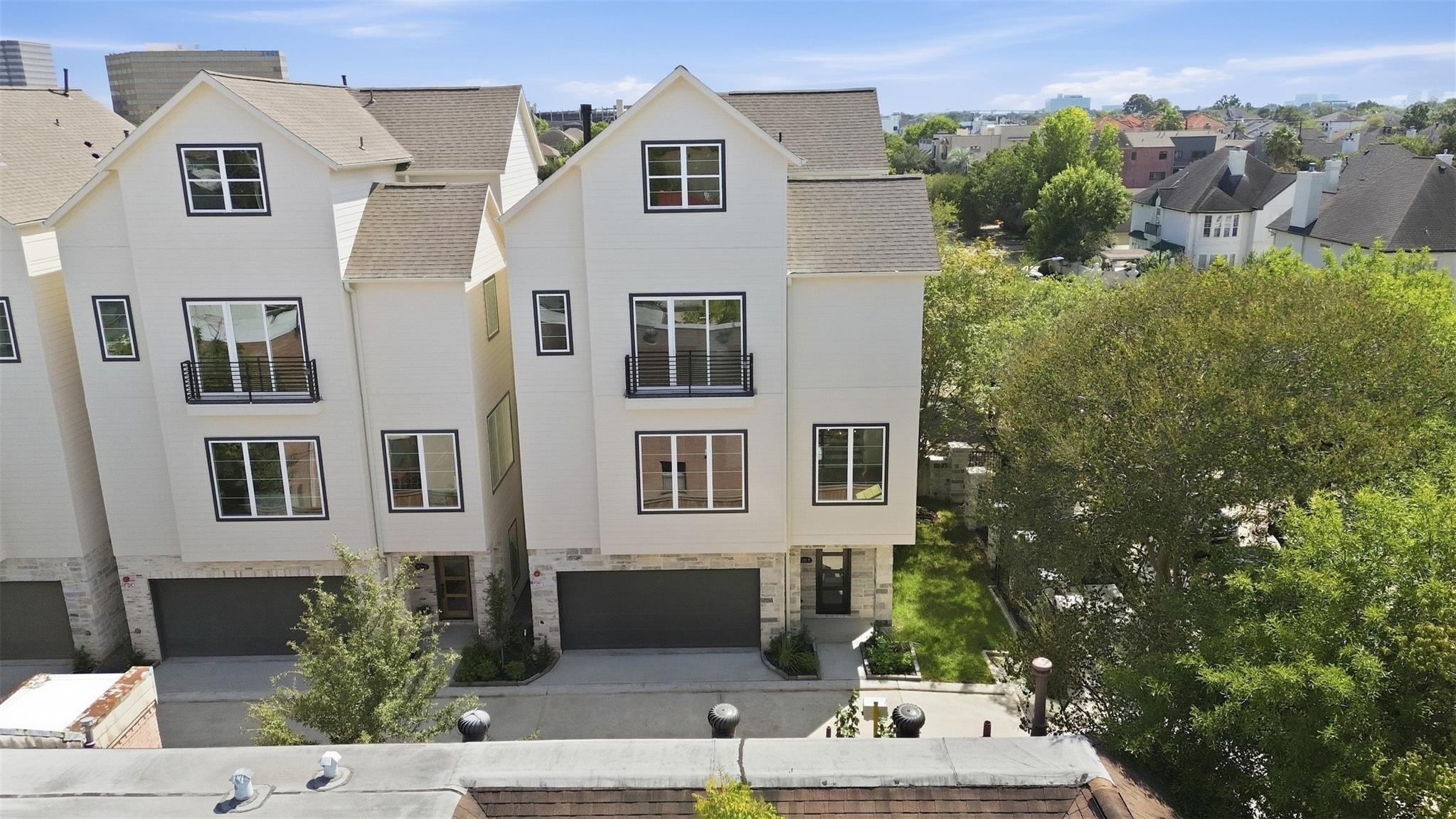 Attached light-colored townhouses with balconies, stone lower façades, and garage doors, seen from above.