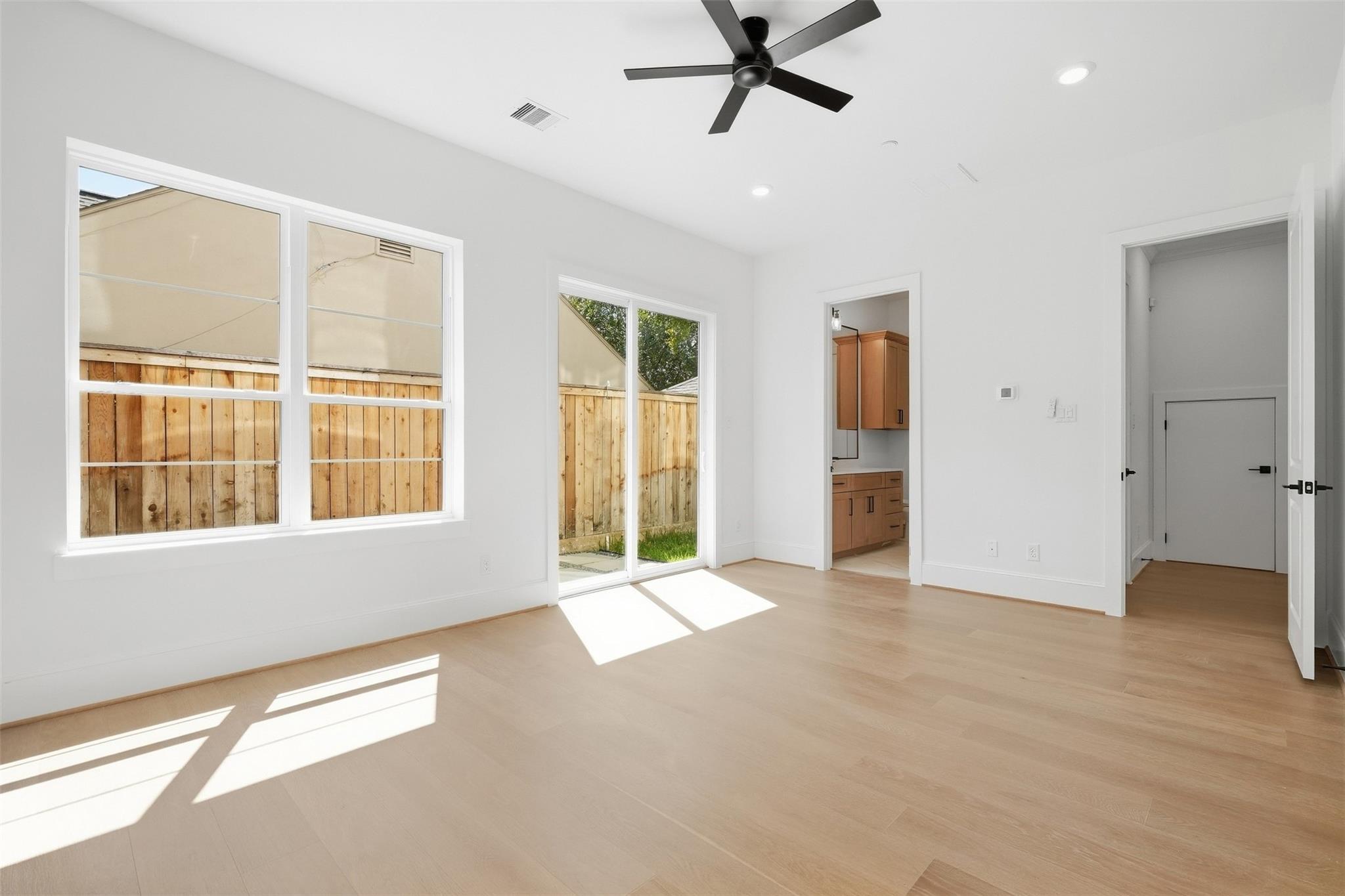 Vacant living area with light wood floors, large windows, and a sliding glass door to the fenced yard.