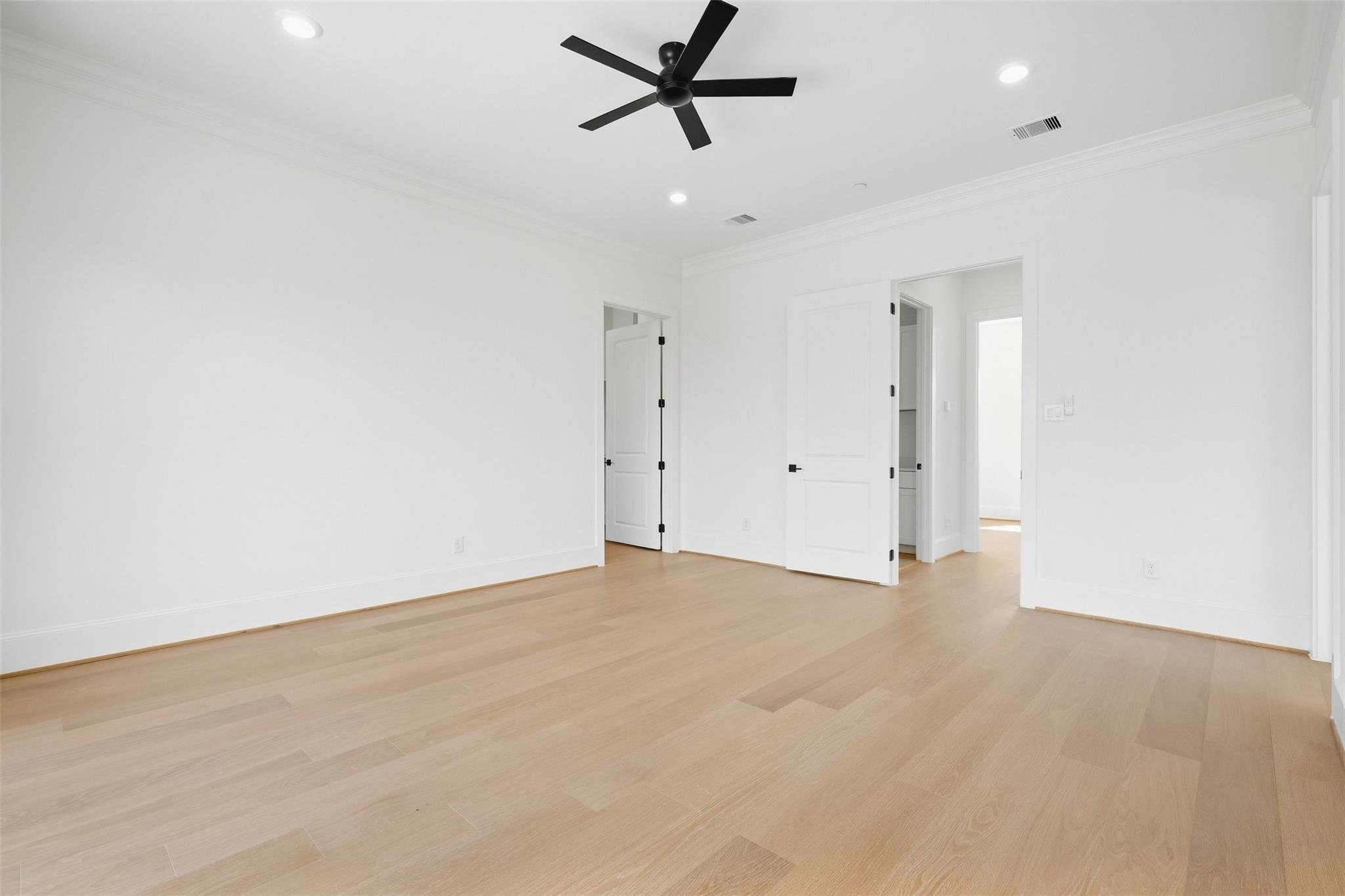 Empty room with light wood floors, white walls, a black ceiling fan, and open doorways.