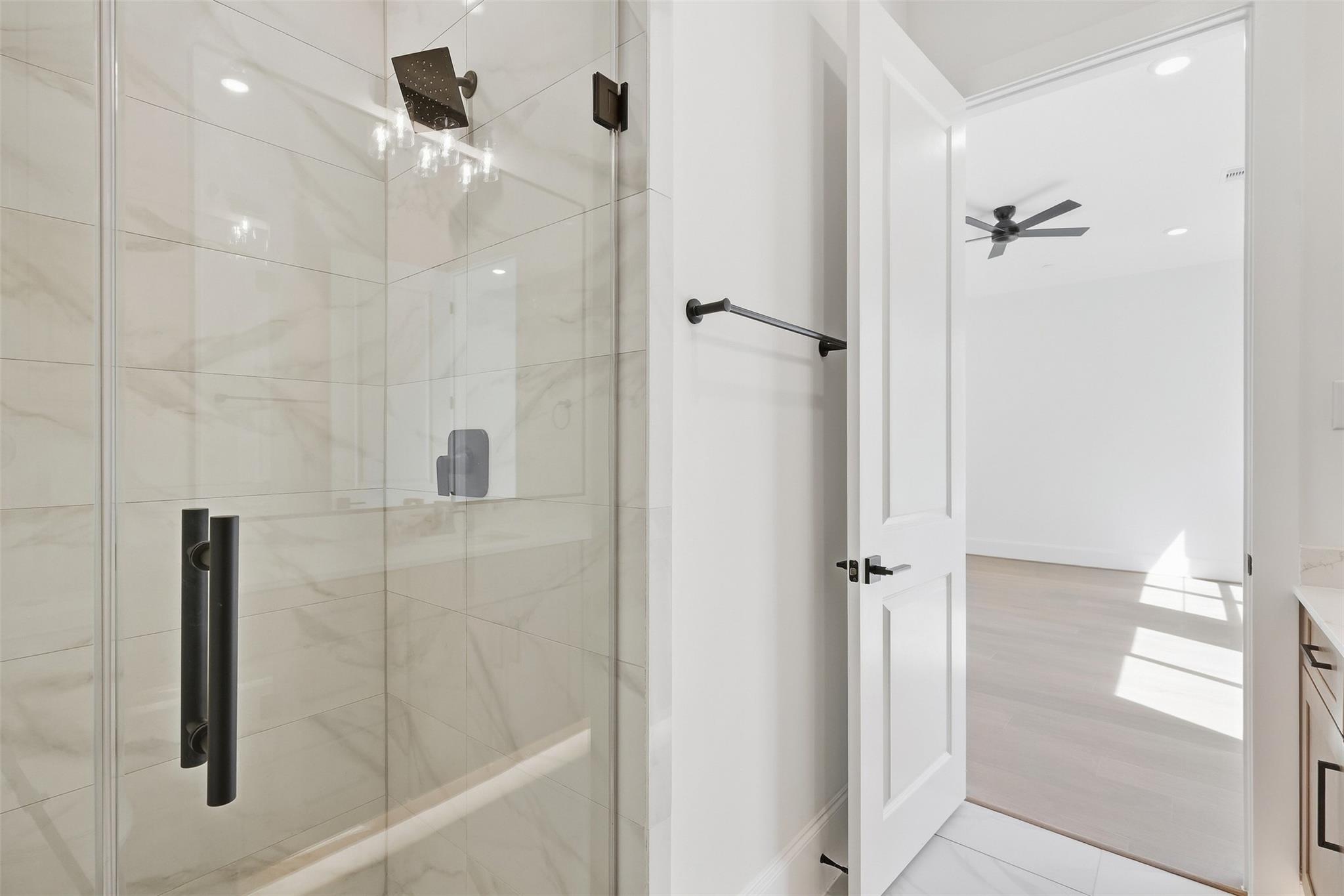 Bathroom with a glass-enclosed, marble-look tiled shower and matte black fixtures.
