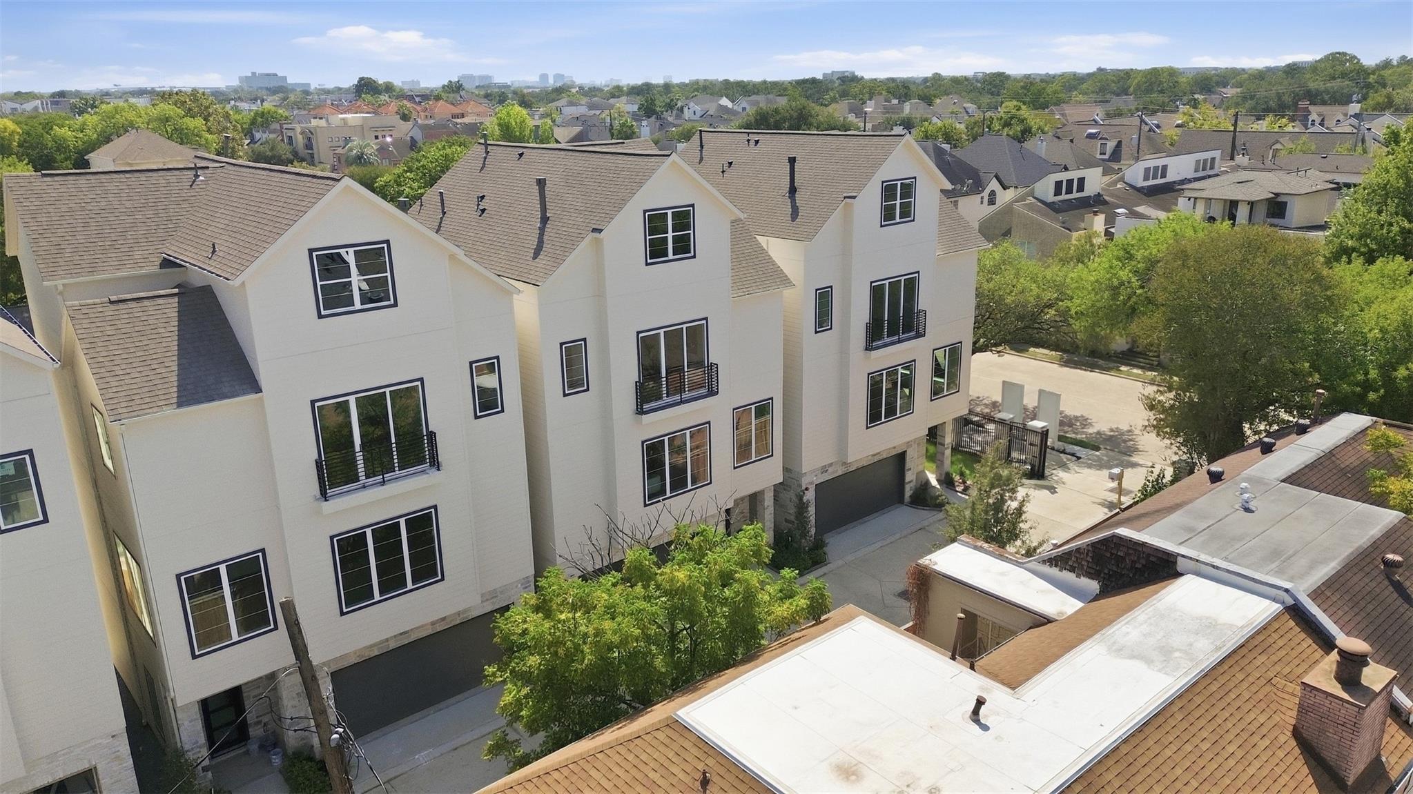 Multi-story townhouse with balconies and driveway, viewed from above with neighborhood homes and skyline beyond.
