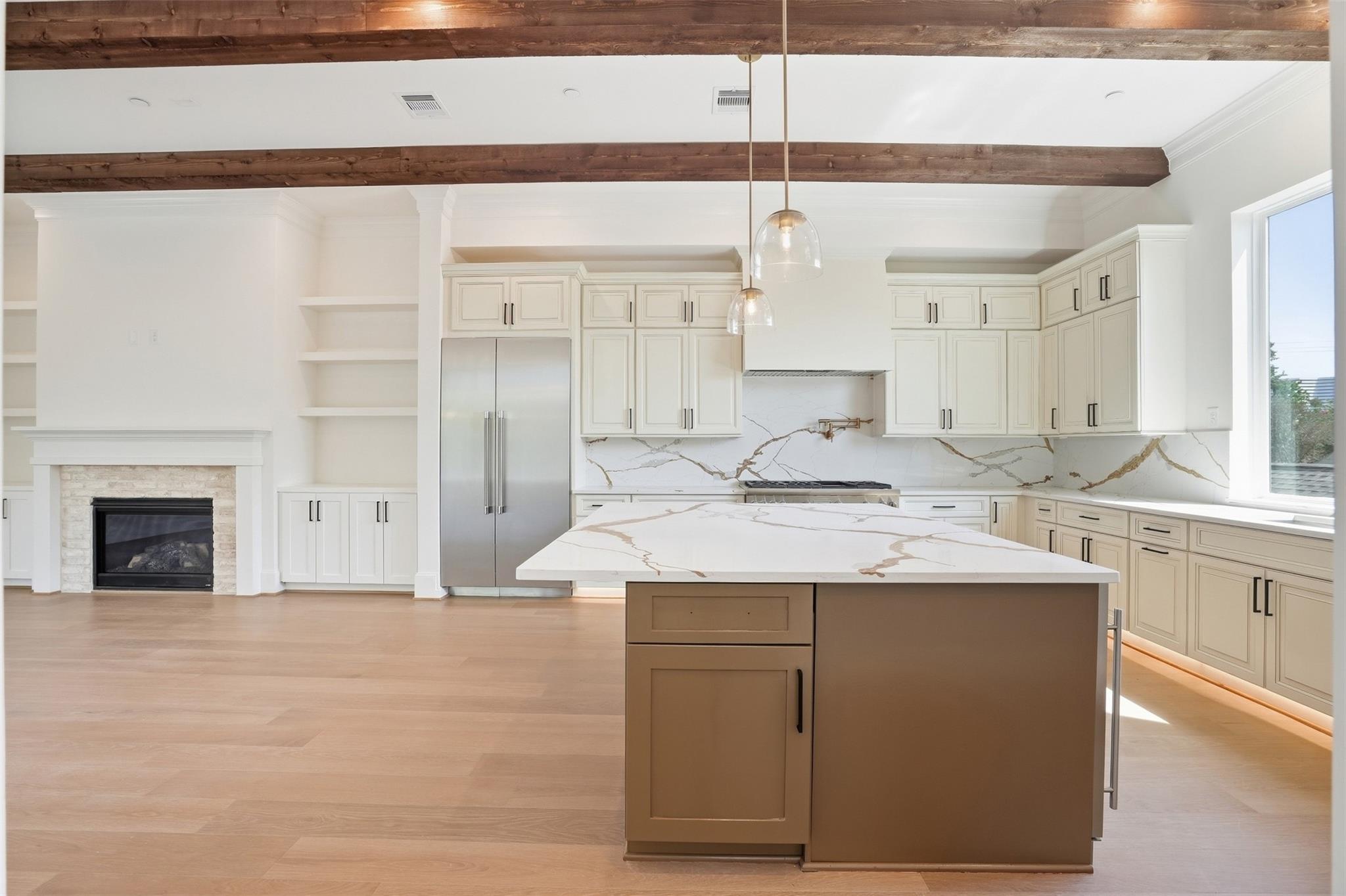 Kitchen with a large veined-stone island, white cabinets, exposed wood beams, and a fireplace.