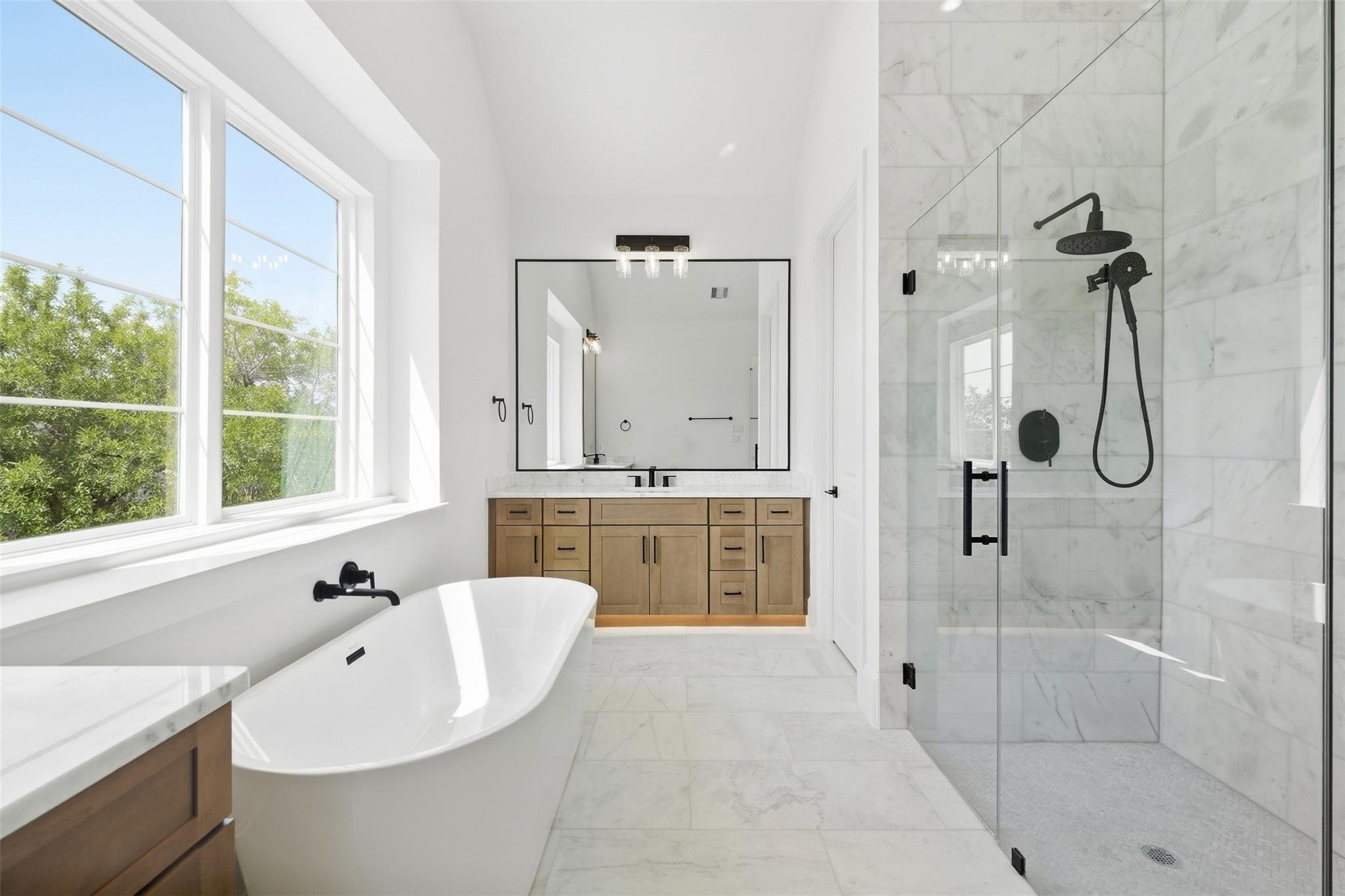 Bright bathroom with a soaking tub, wood vanity, and glass-enclosed marble shower.
