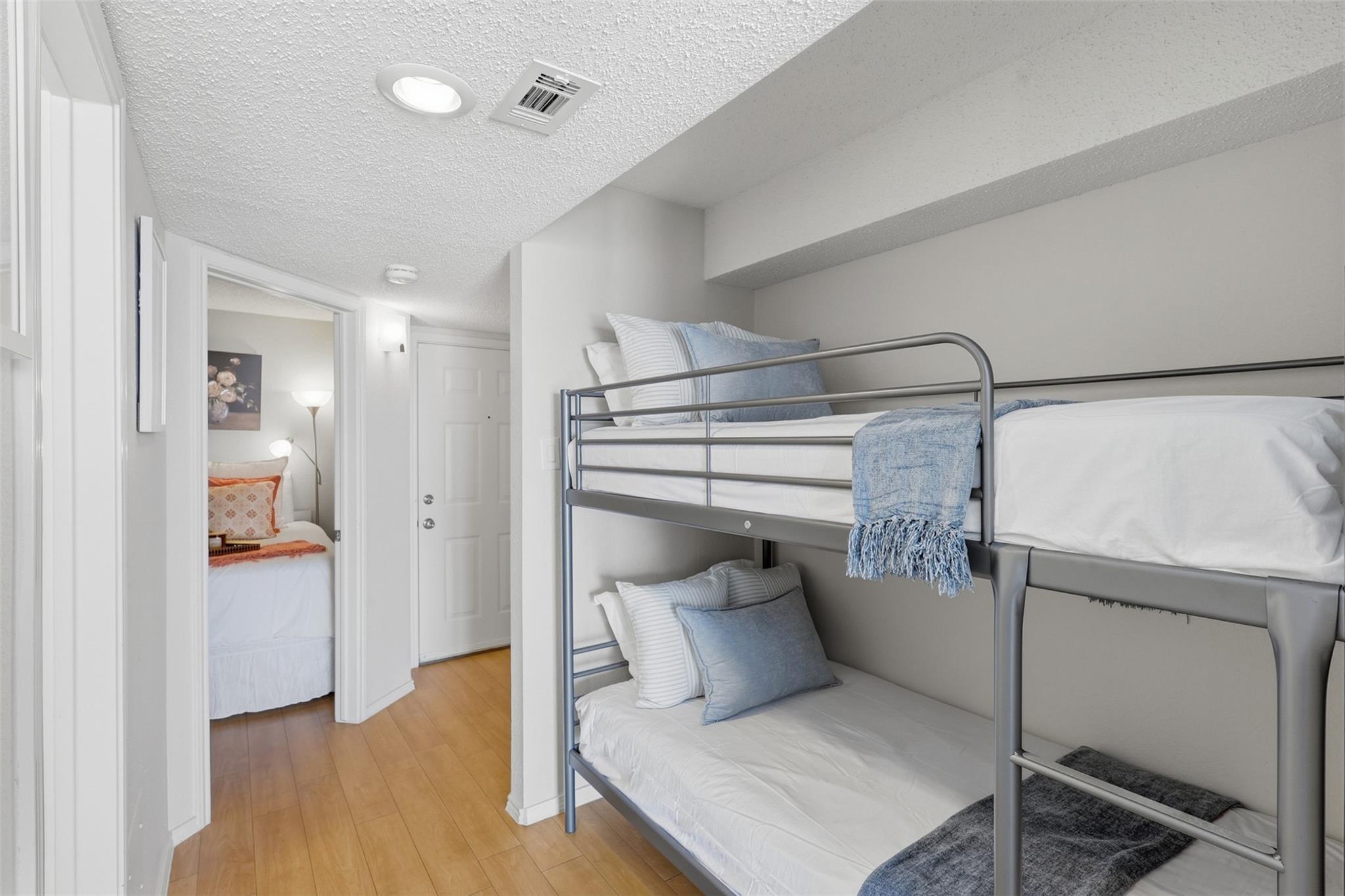 Bedroom with a gray metal bunk bed and blue bedding, with another bedroom visible through the doorway.
