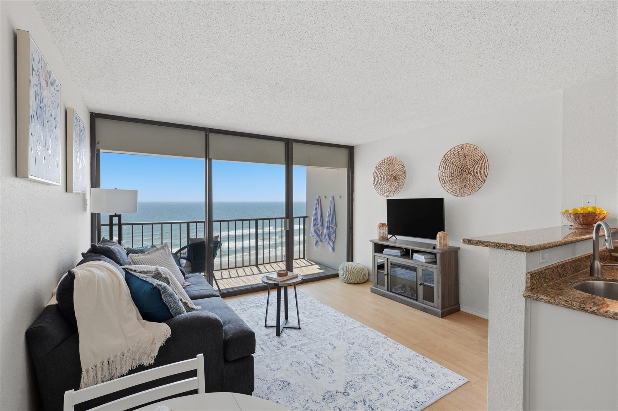 Furnished condo living room with sliding glass doors overlooking the ocean and balcony.