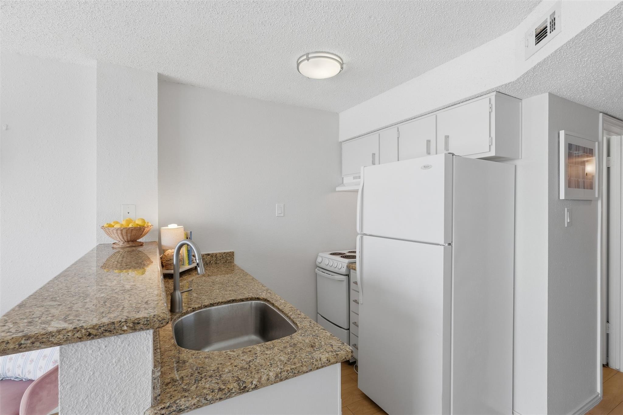 Compact kitchen with granite counters, white appliances, and a stainless steel sink in the peninsula.