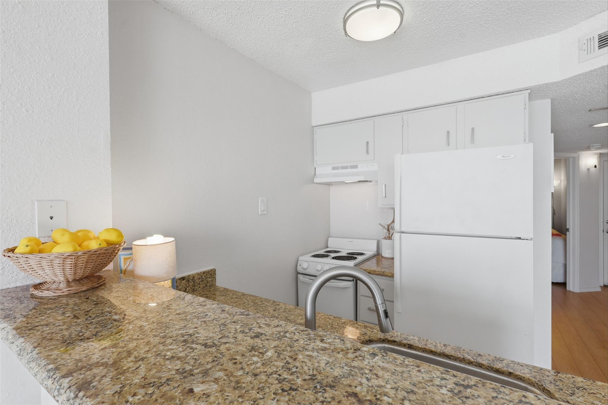 Compact kitchen with granite counters, a breakfast bar sink, and white appliances.