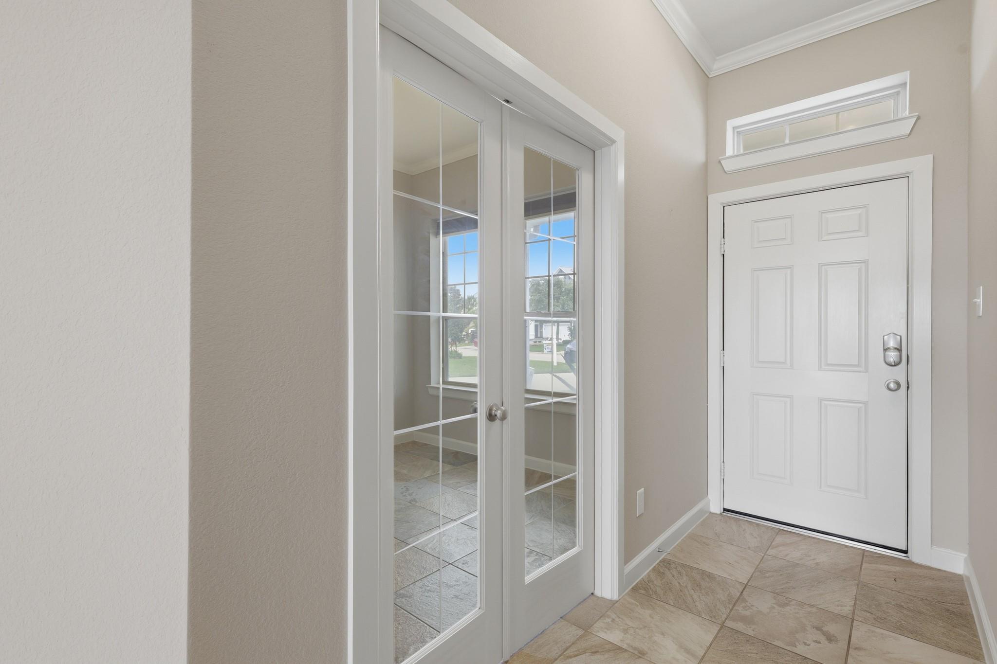 Entry foyer with a white front door and glass-paneled French doors opening to a tiled room.