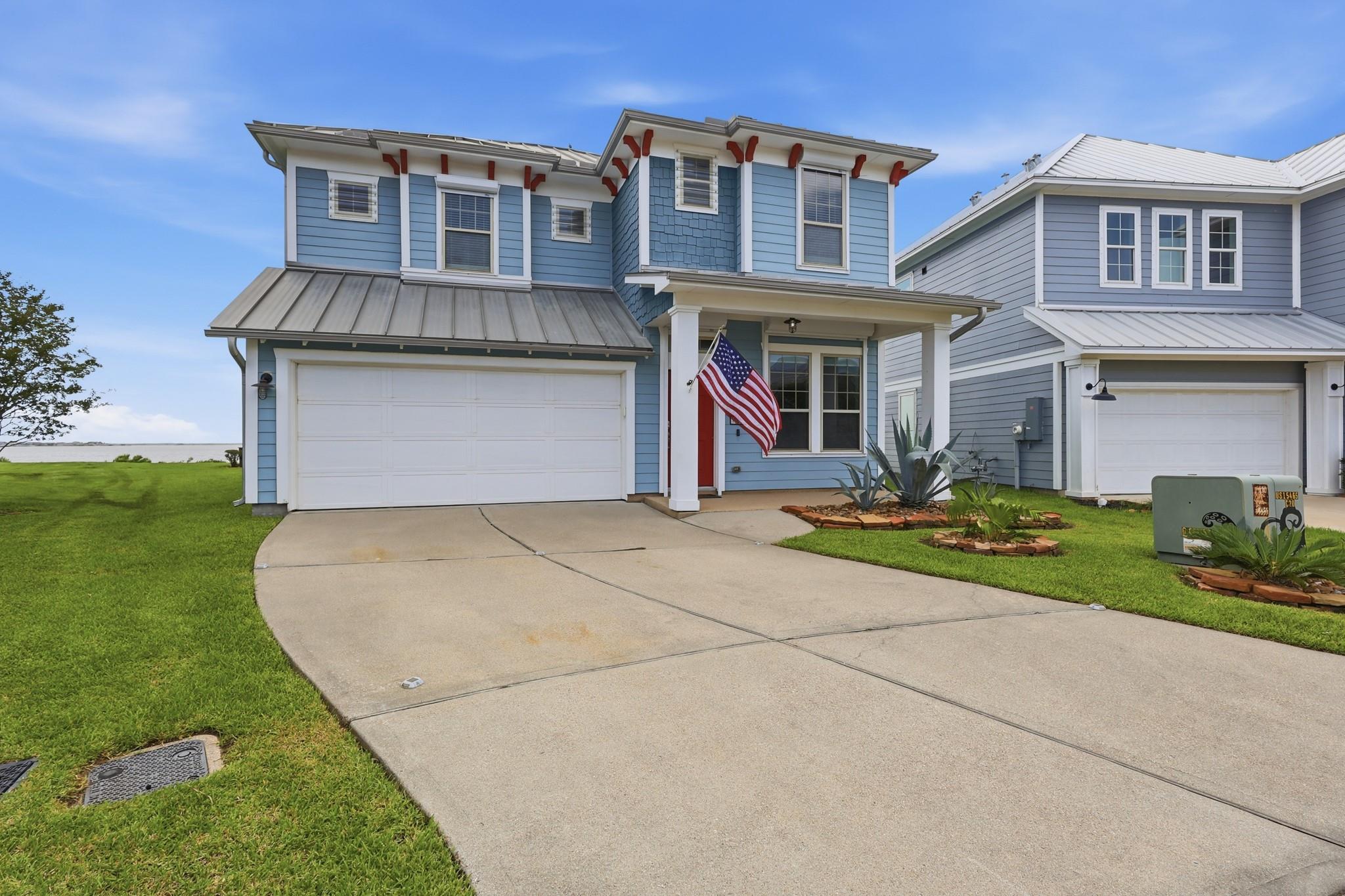 Blue two-story house with a wide driveway, white trim, and an American flag by the entrance.