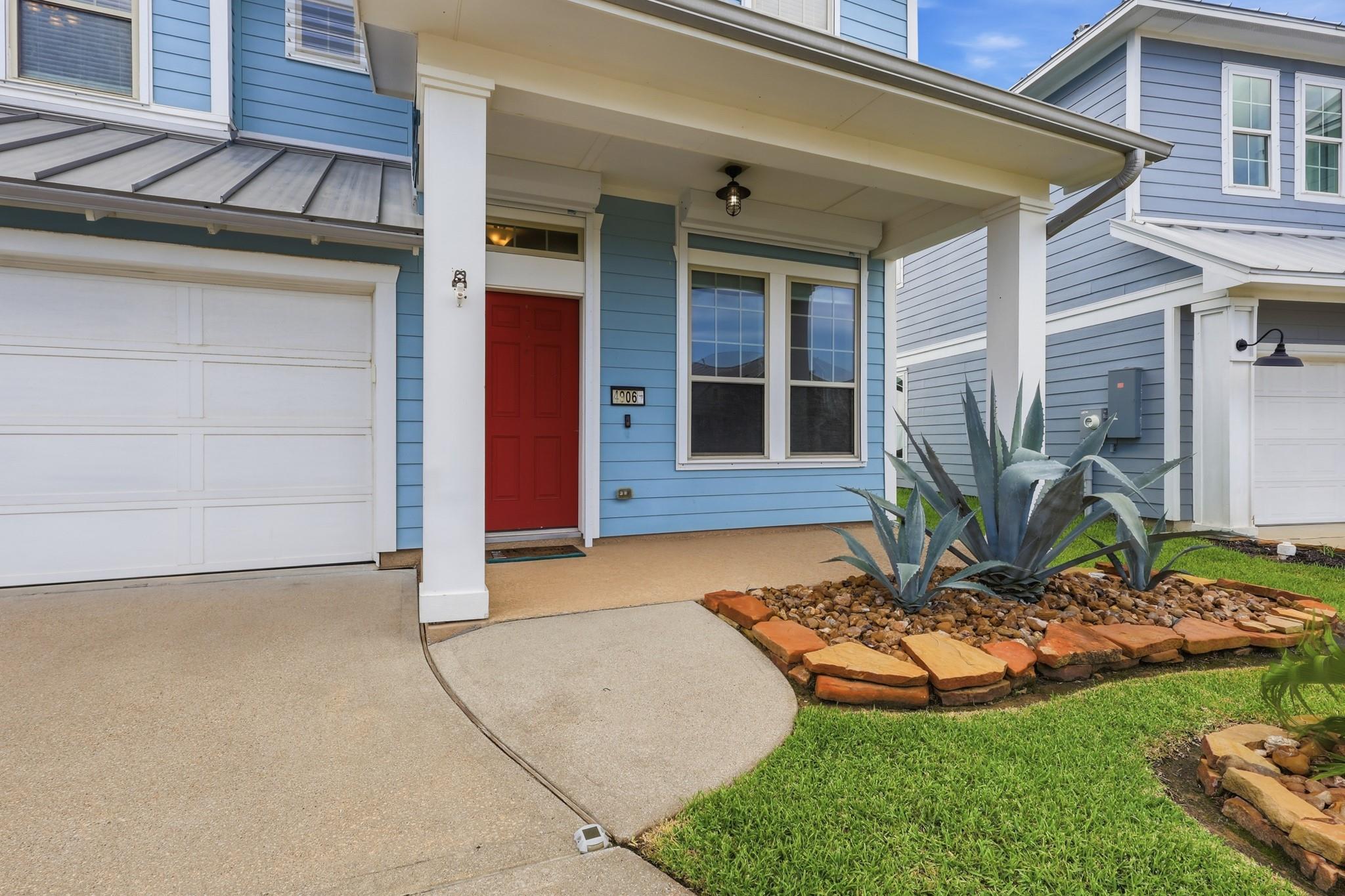 Blue two-story house with a red front door, covered porch, and agave rock garden.