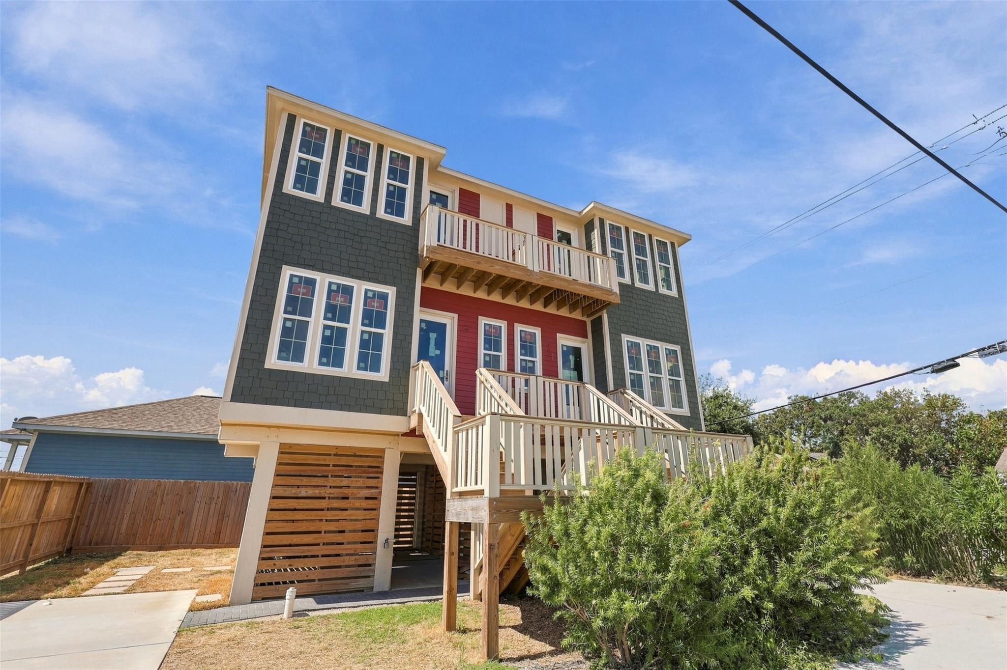 Elevated house with red and dark gray siding, a balcony, exterior stairs, and a covered area below.