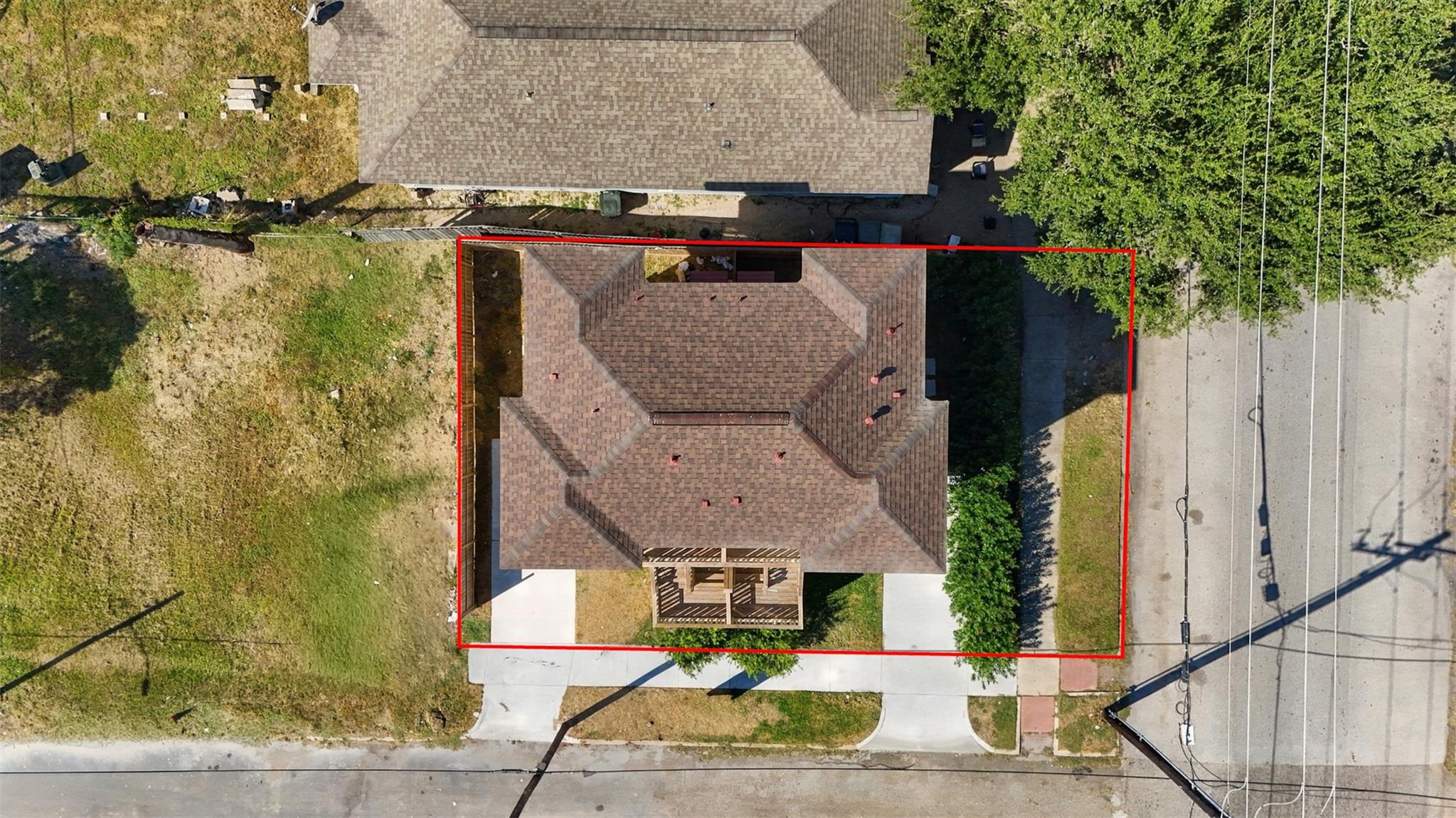 Aerial view of a house and lot outlined in red, with a brown shingle roof and front porch.