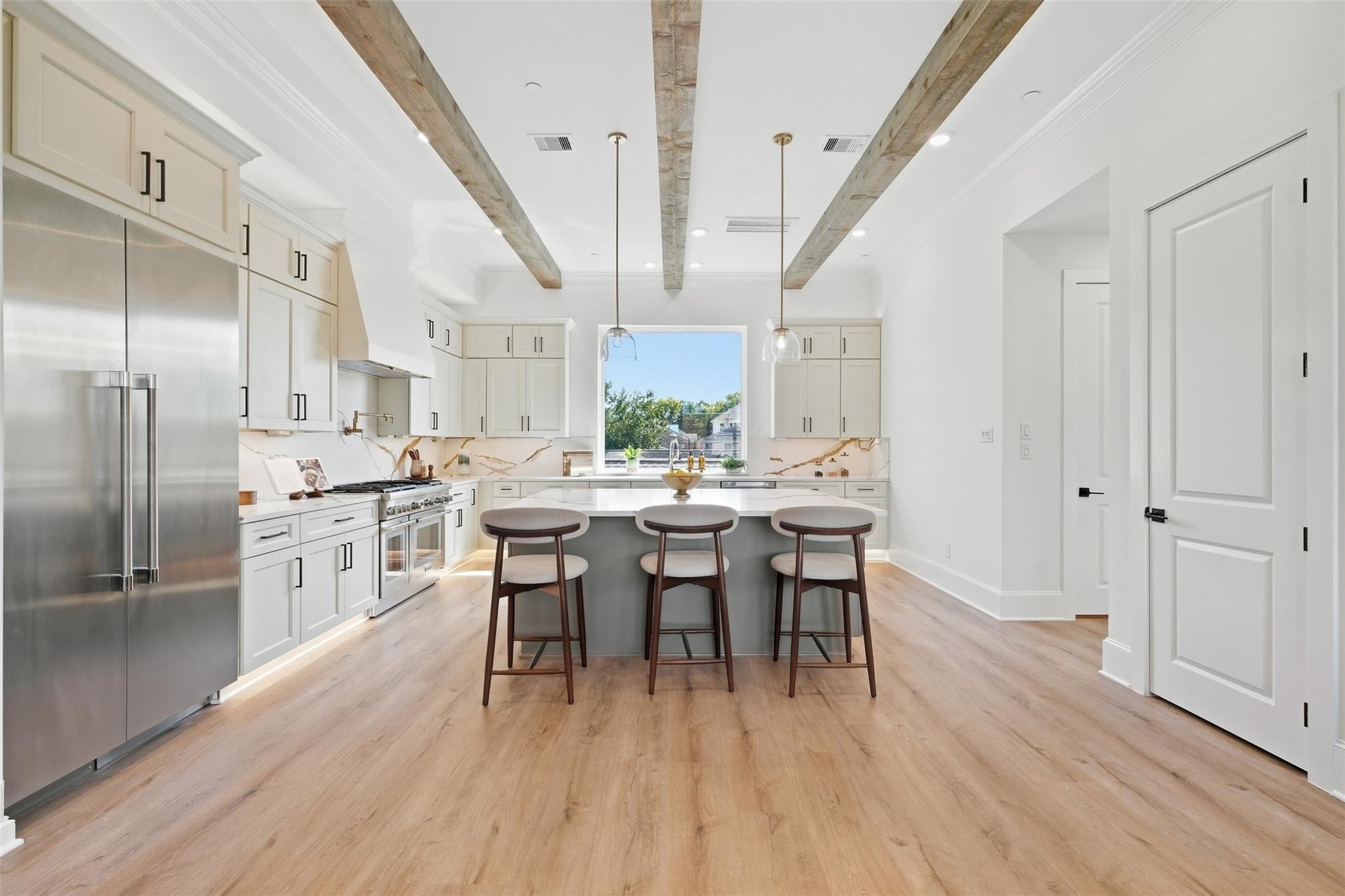 Bright white kitchen with exposed wood ceiling beams and a gray island with three stools.