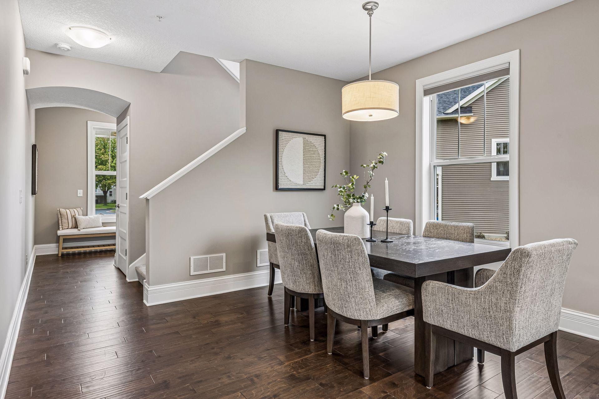 Staged dining room with a dark table, upholstered chairs, and an arched hallway opening.