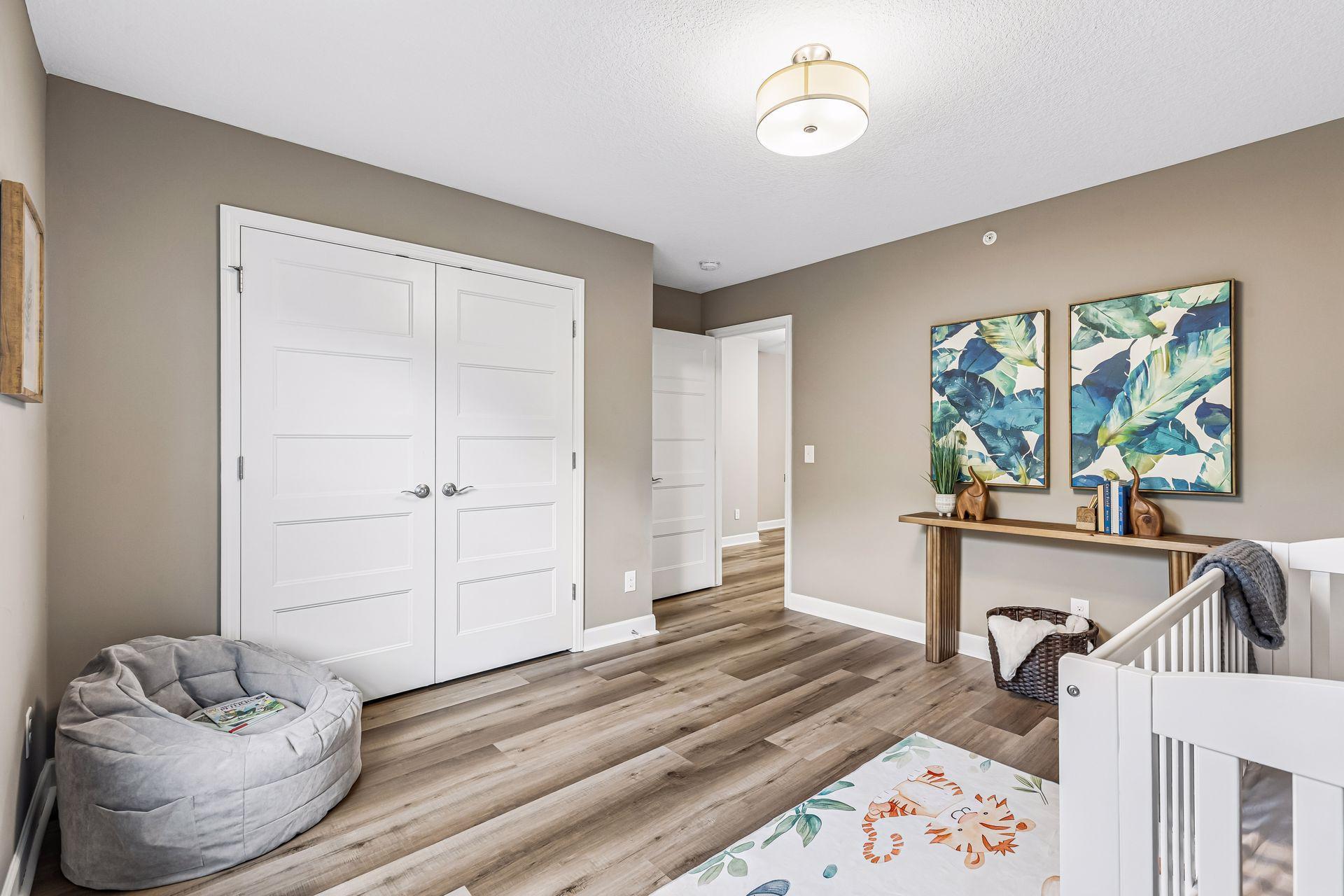 Nursery with a white crib, gray floor cushion, wood-look flooring, and colorful botanical art.
