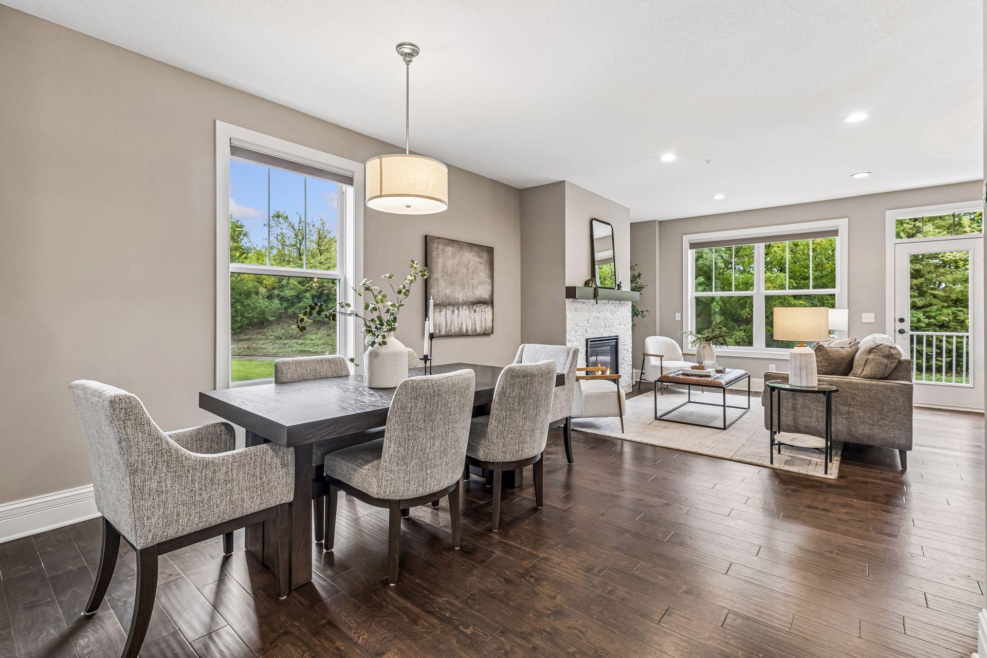 Open-plan dining and living room with a dark wood table, white brick fireplace, and large windows.