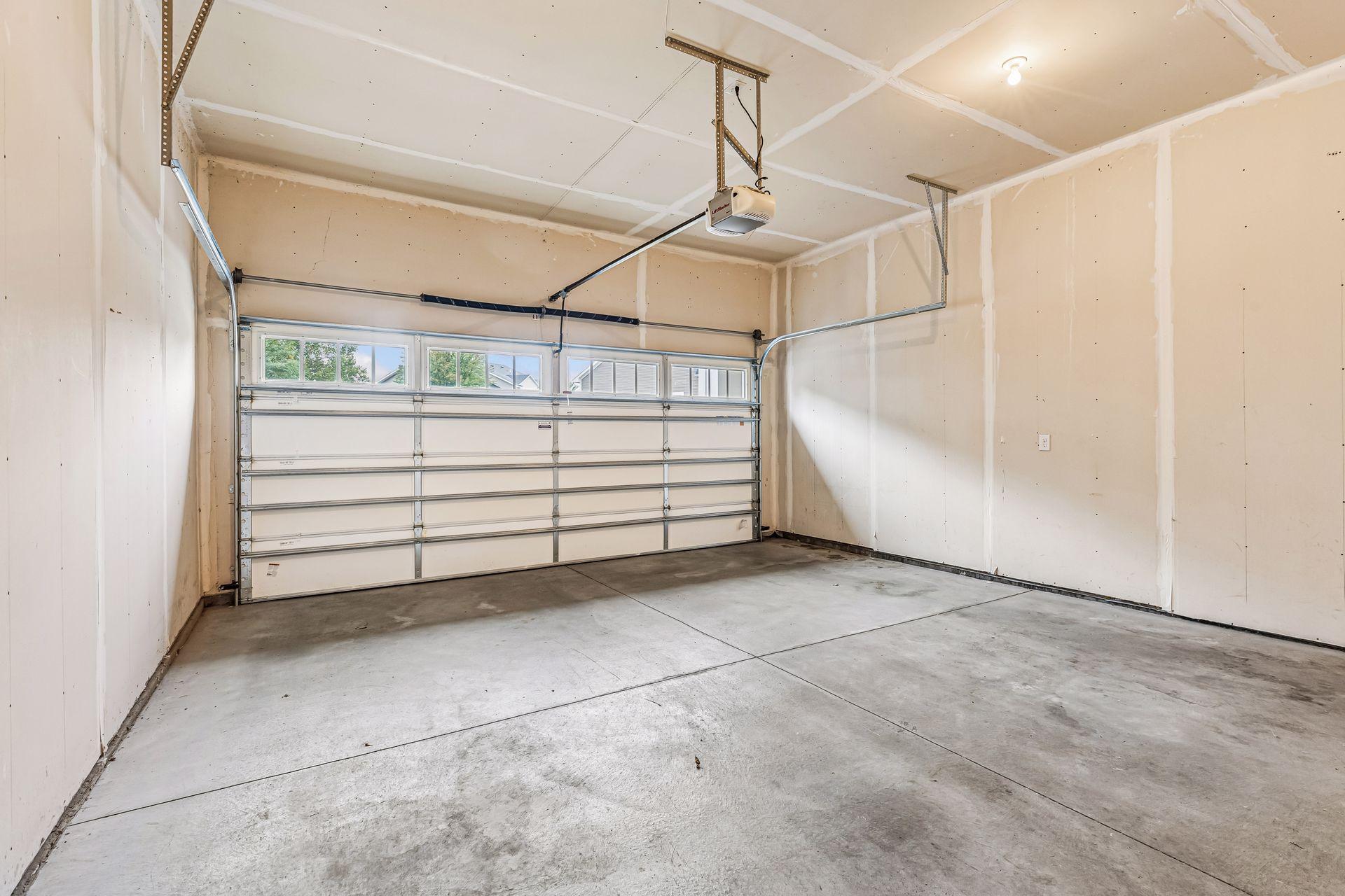 Empty garage with a concrete floor, ceiling-mounted opener, and overhead door with windows.