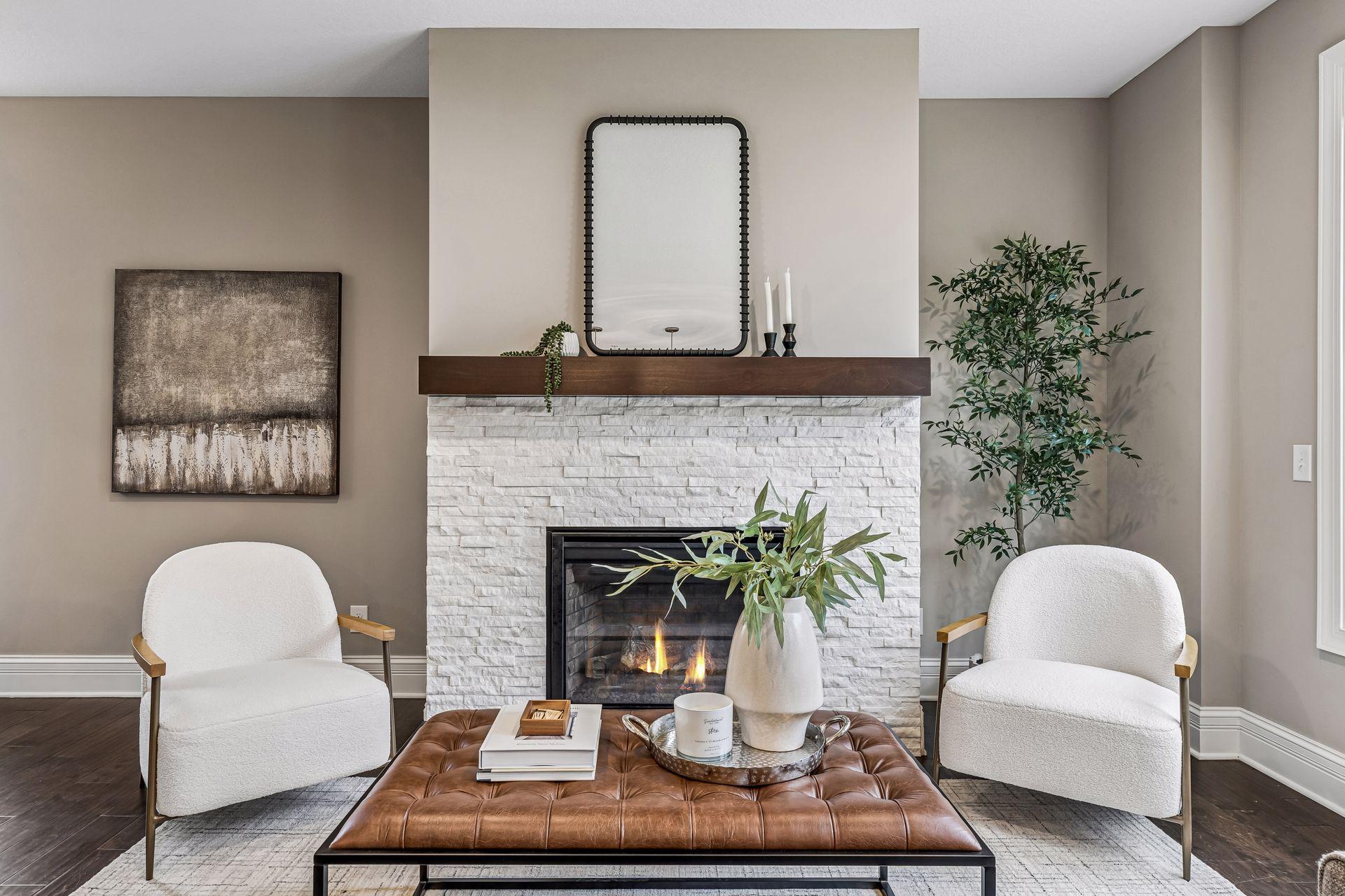 Staged living room with a white stone fireplace, dark wood mantel, and two white armchairs.