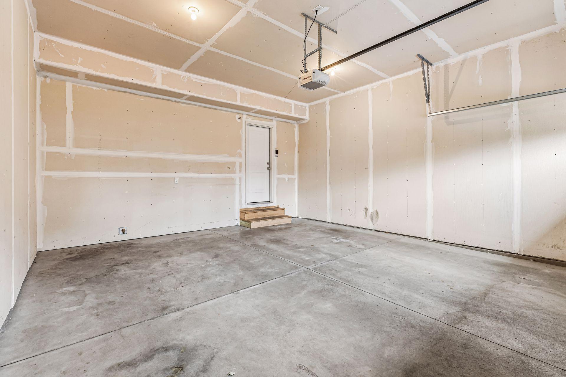 Unfinished garage with taped drywall, a concrete floor, and a ceiling-mounted door opener.