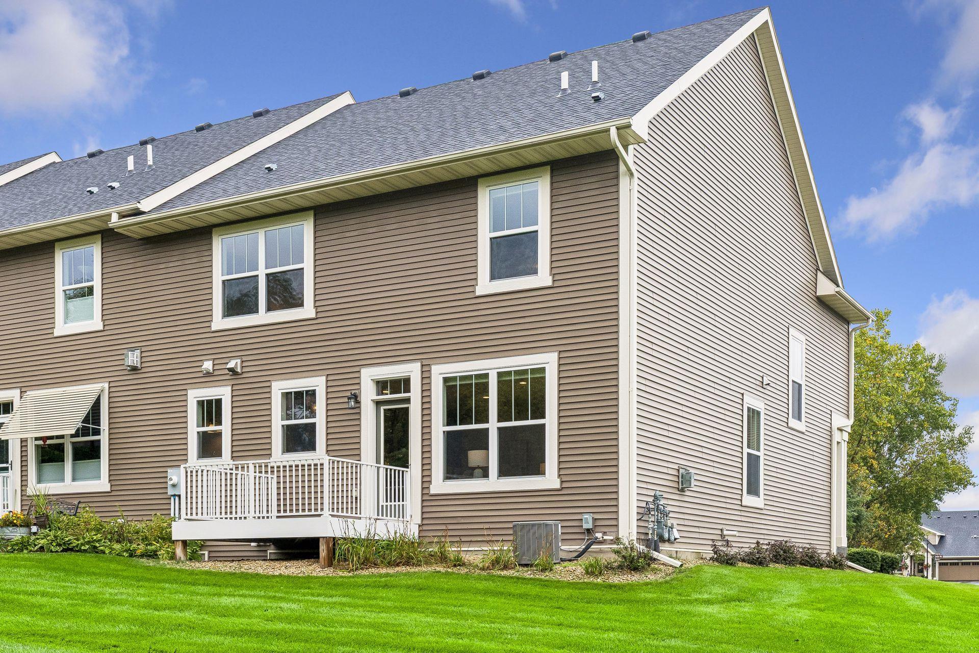 Two-story townhouse with brown siding, white trim, and a small rear deck beside a green lawn.