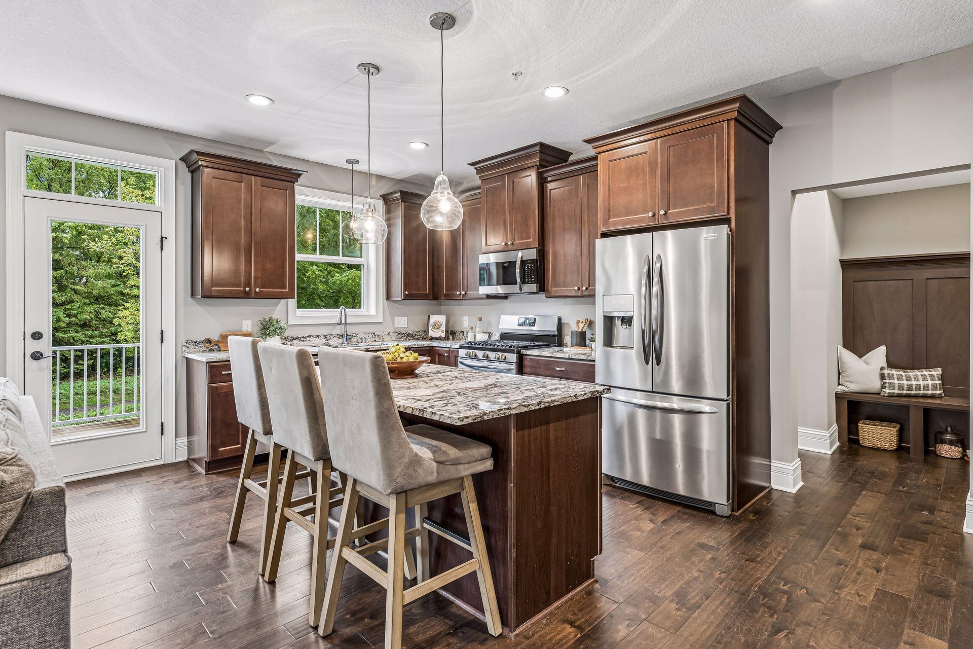 Kitchen with dark wood cabinets, stainless appliances, and a granite island beside a glass door to leafy greenery.