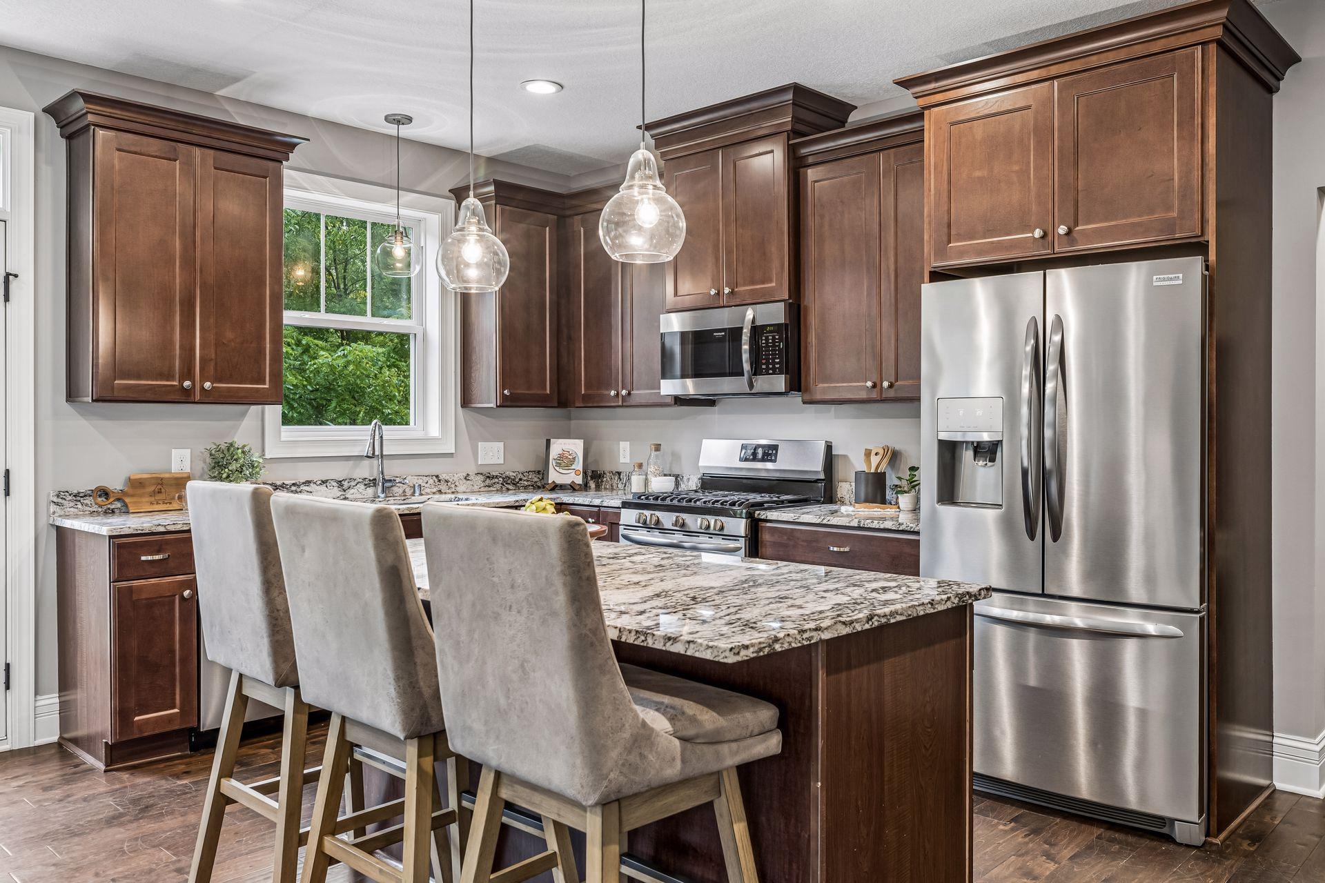 Kitchen with dark cherry cabinets, granite island, upholstered stools and stainless steel appliances.