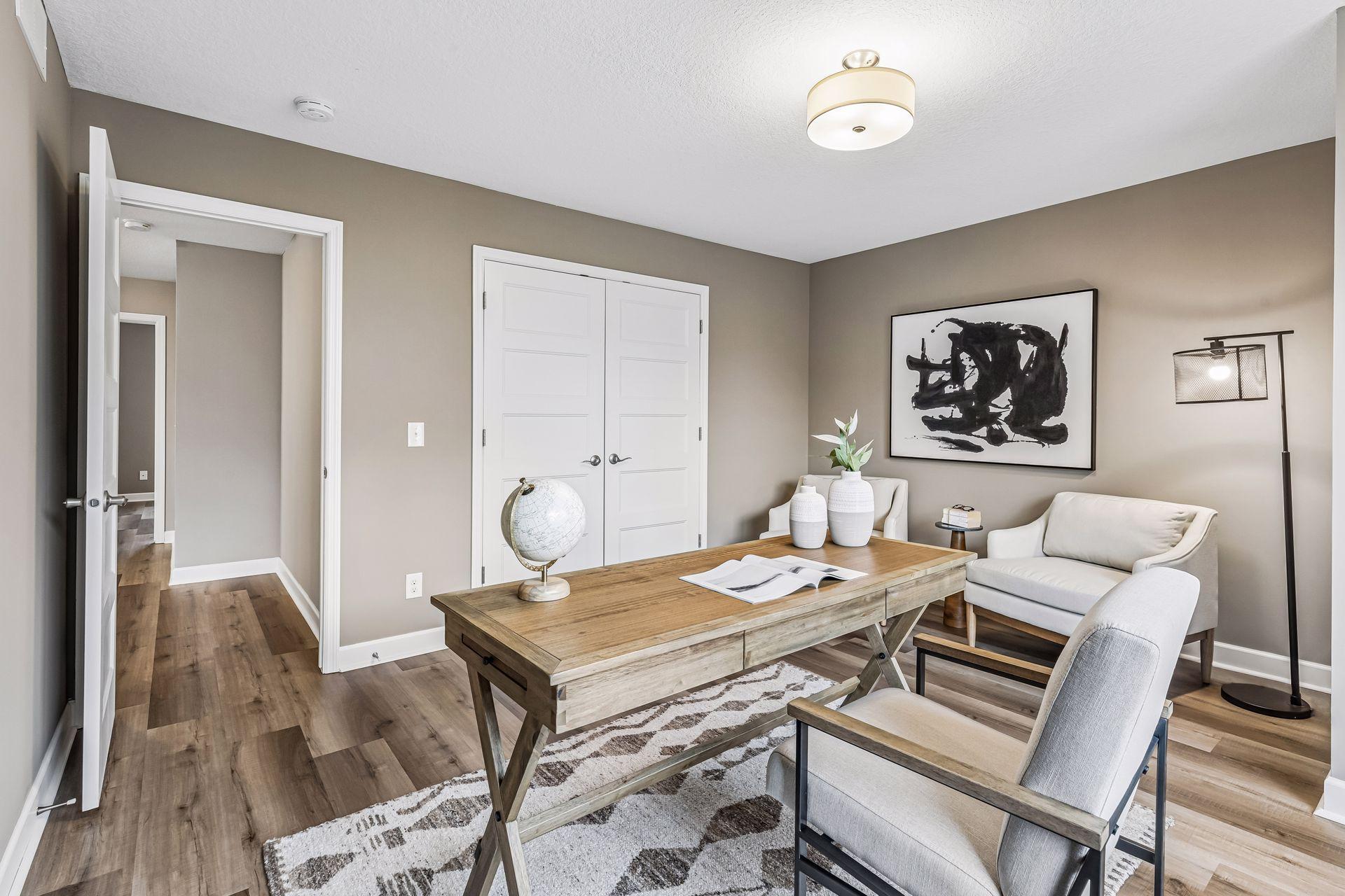 Staged home office with a large wooden desk and two light upholstered chairs.