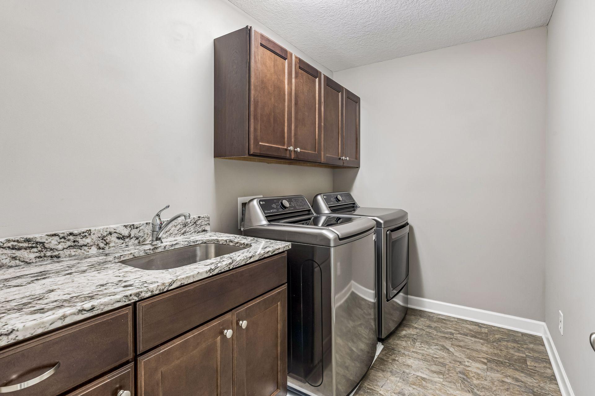 Laundry room with a top-load washer and dryer beside dark cabinets and a granite utility sink.