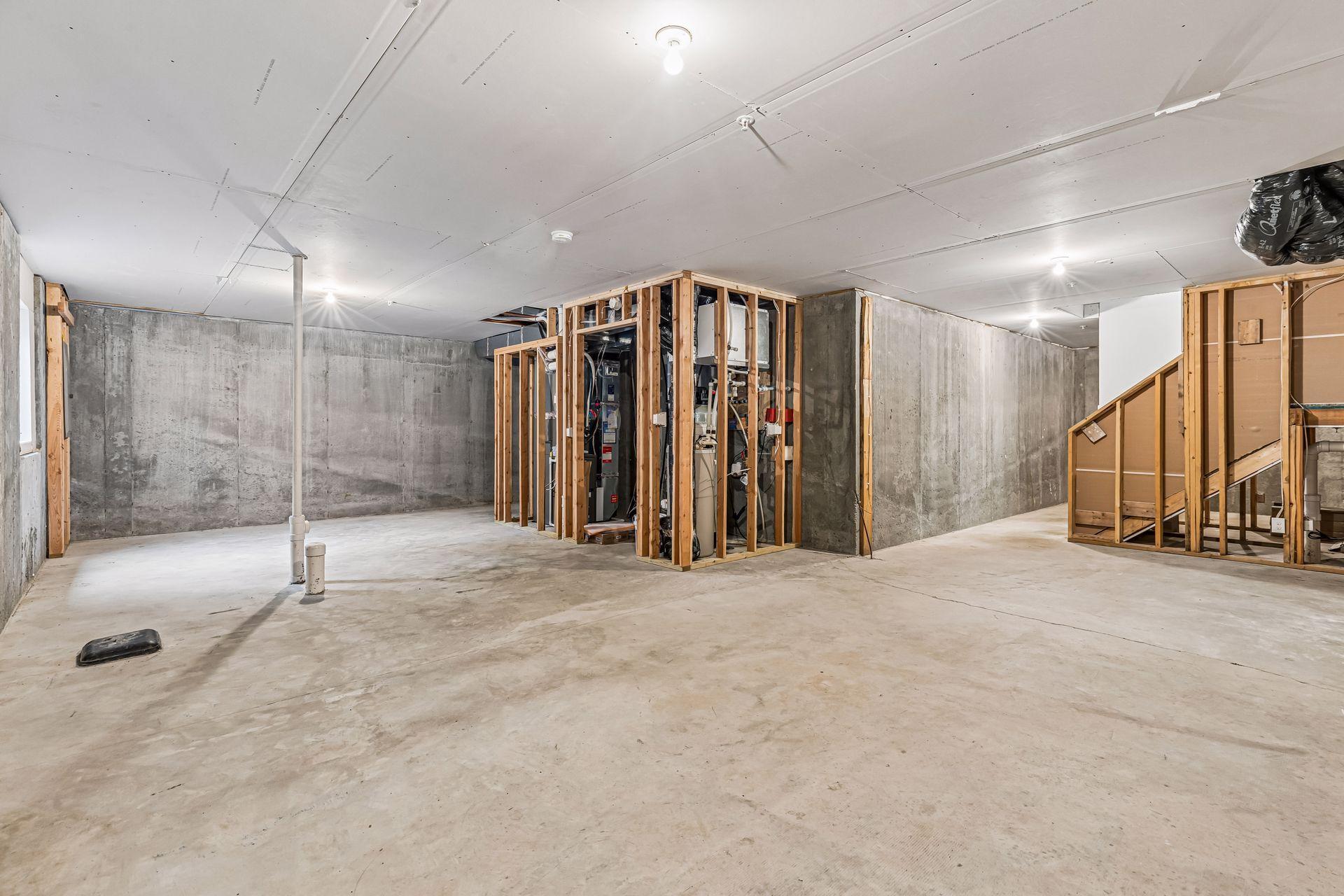 Unfinished basement with exposed concrete walls, framed mechanical area, and an open staircase.