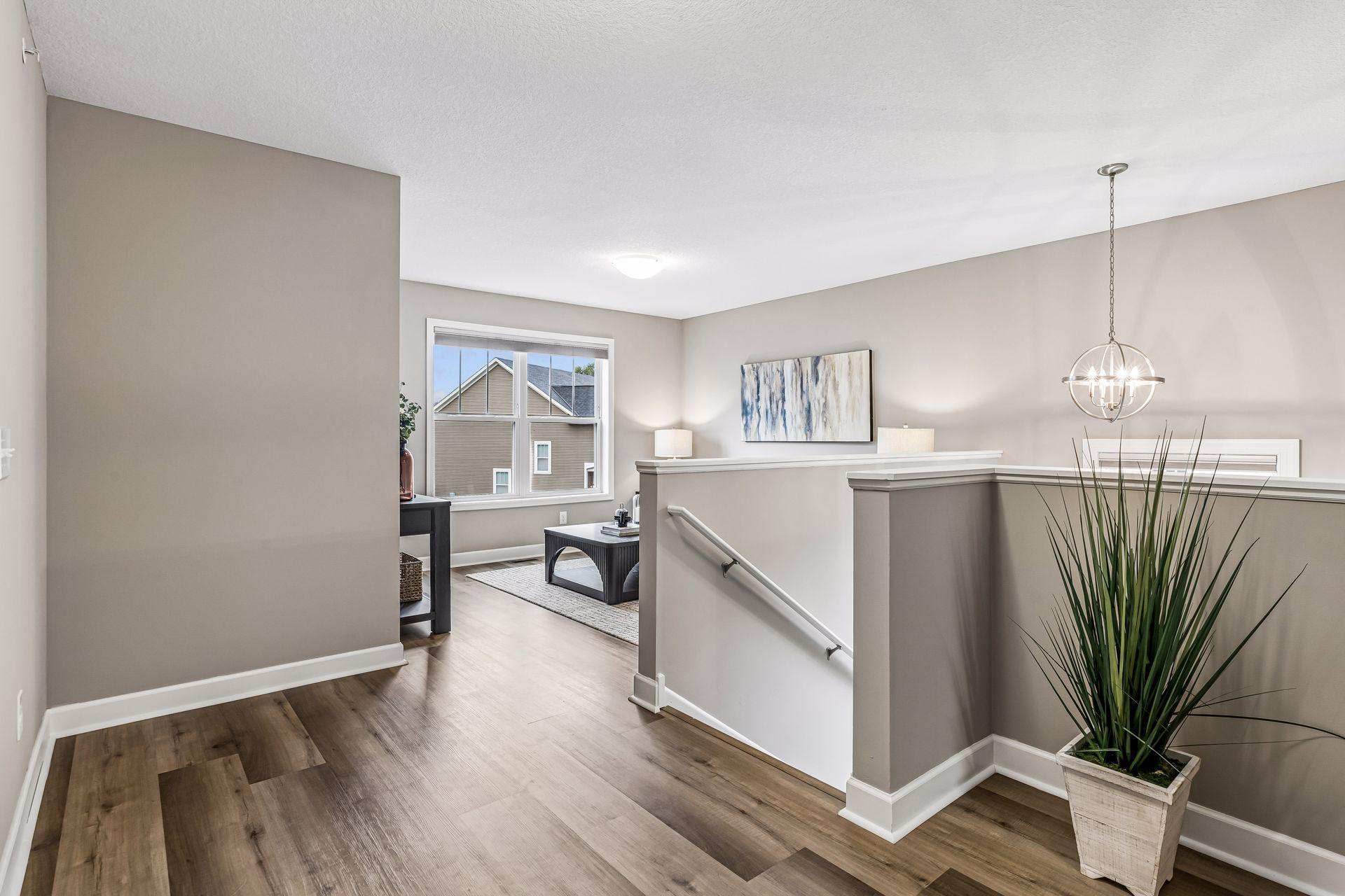 Furnished upstairs living area beside an open stairwell, with wood-look flooring and a large window.