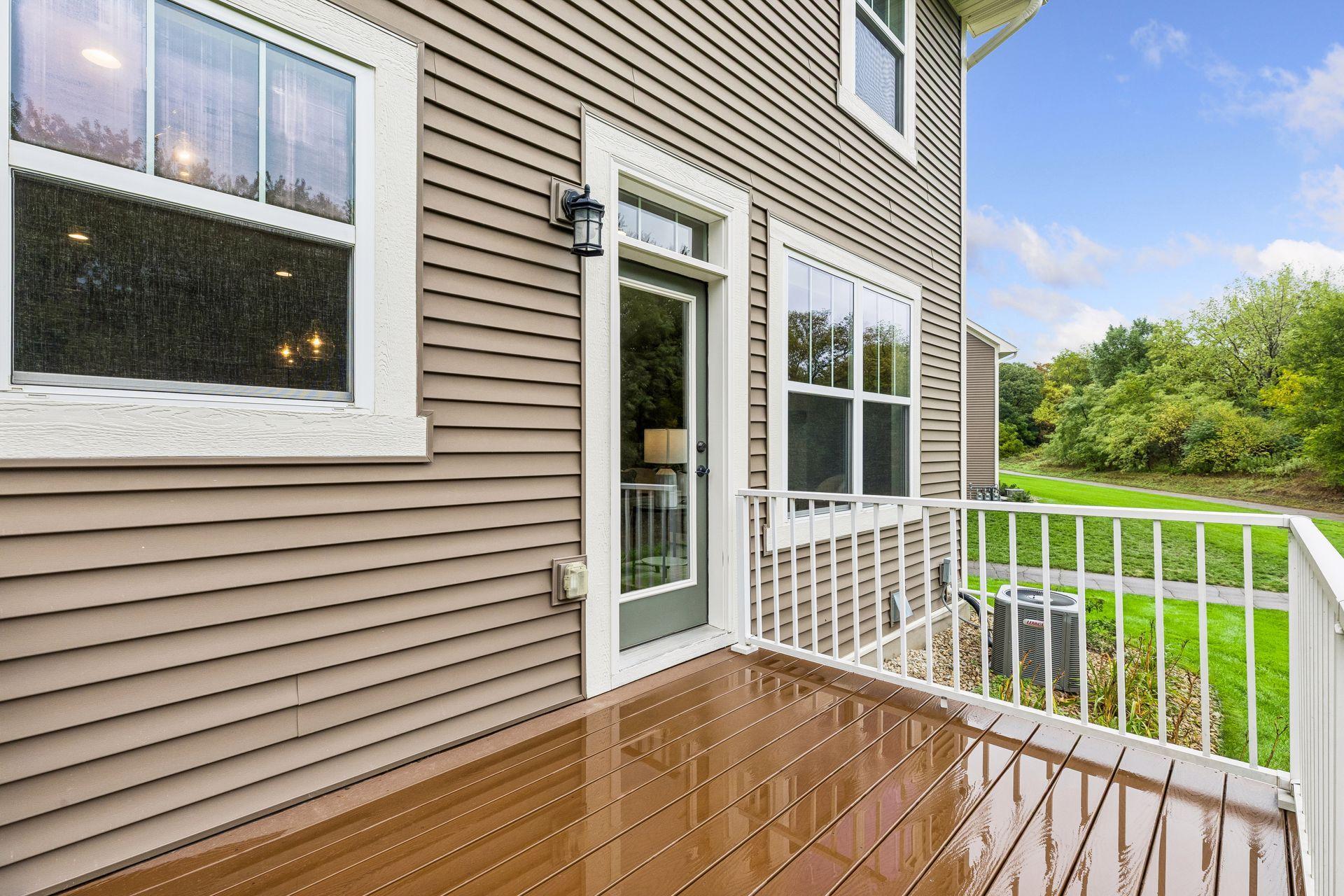 Brown-sided home with a wet wooden deck and white railing overlooking a green lawn.