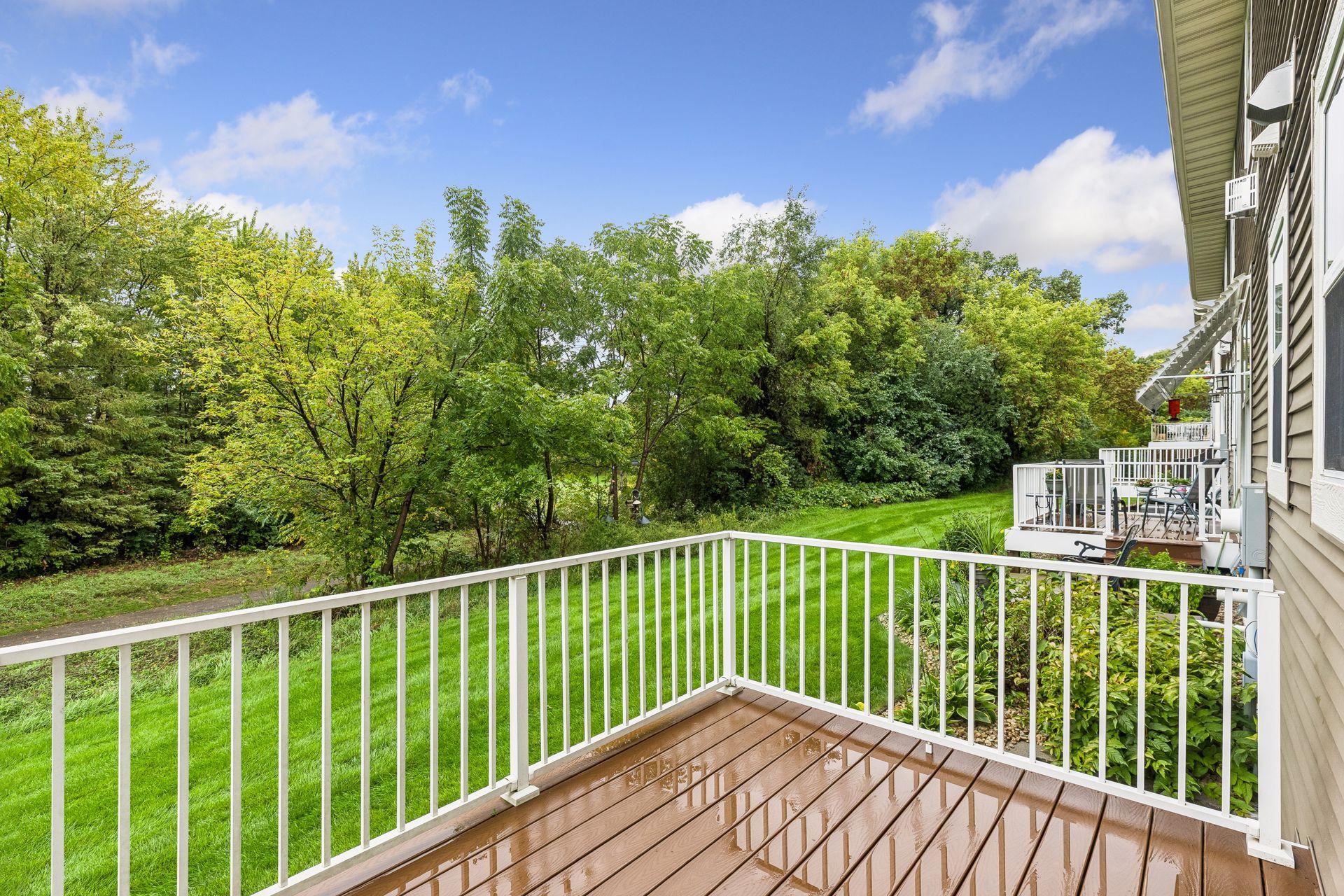 Wooden deck overlooking a green lawn and dense trees, with neighboring townhouse patios along the side.