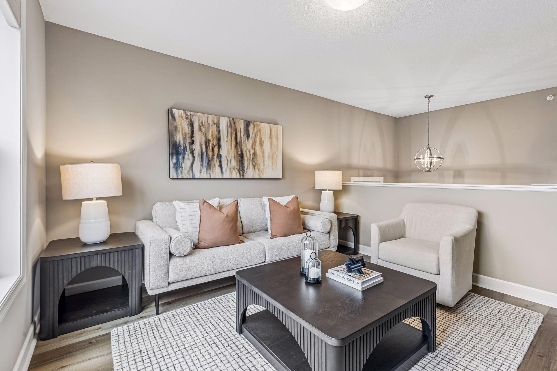 Staged living room with a gray sofa, white armchair, and dark coffee table beneath abstract wall art.