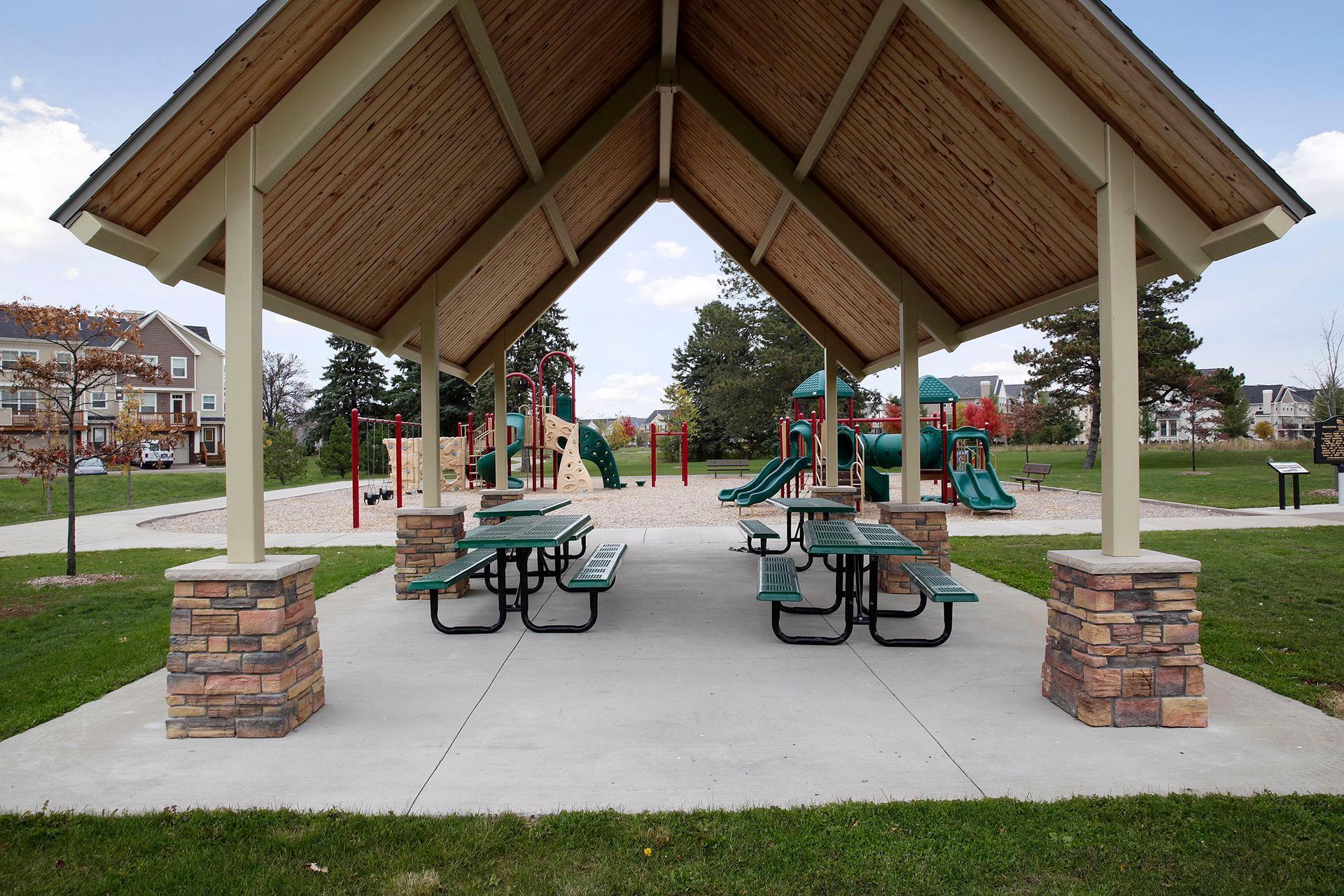 Neighborhood playground under a timber pavilion, with picnic tables and colorful play equipment.