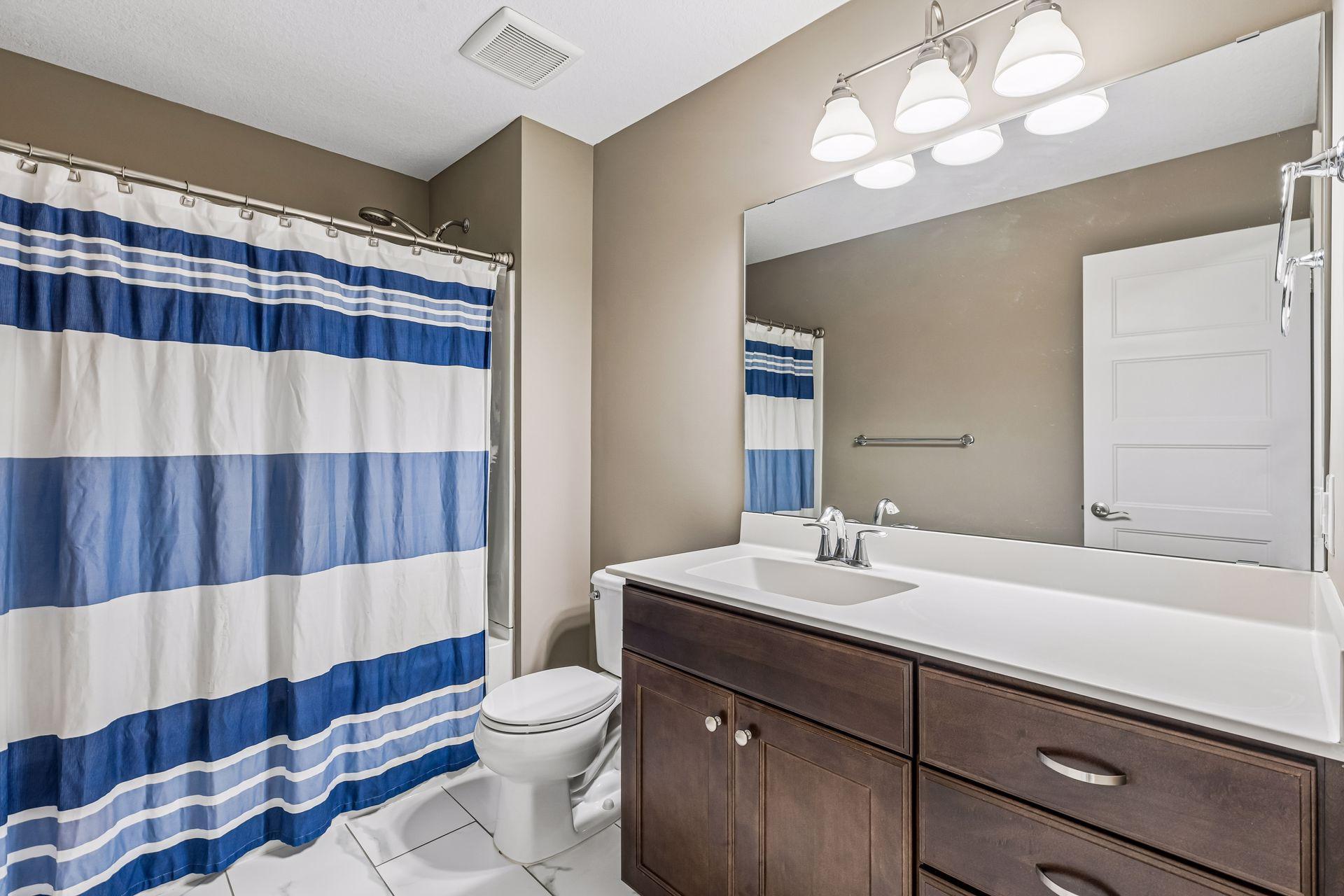 Bathroom with a dark wood vanity, large mirror, and blue-and-white striped shower curtain.