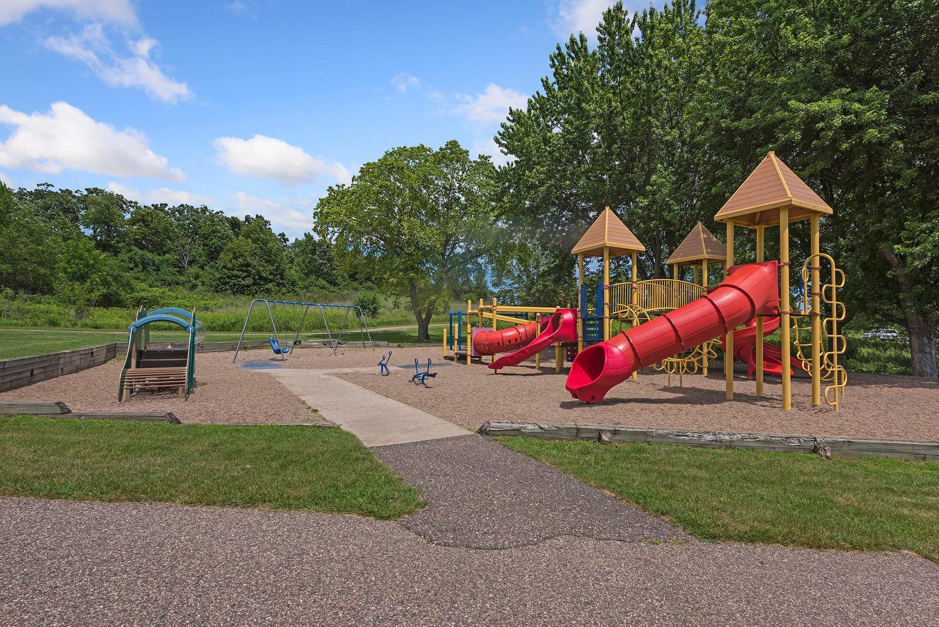 Neighborhood playground with red tube slides, swings, and leafy trees.